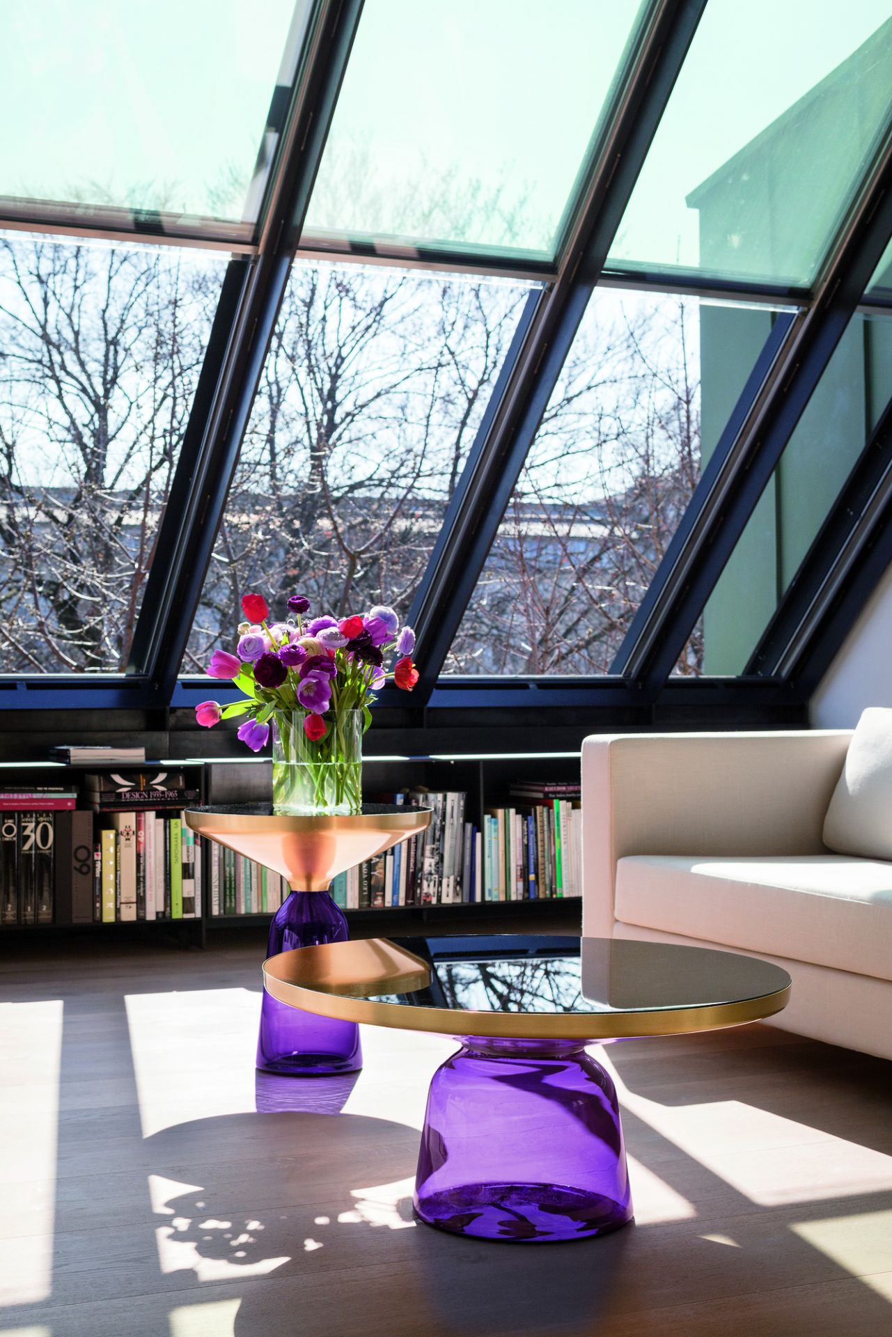Bell Coffee Table Couchtisch von ClassiCon mit violetter Glasbasis und Messingplatte im modernen Wohnzimmer.