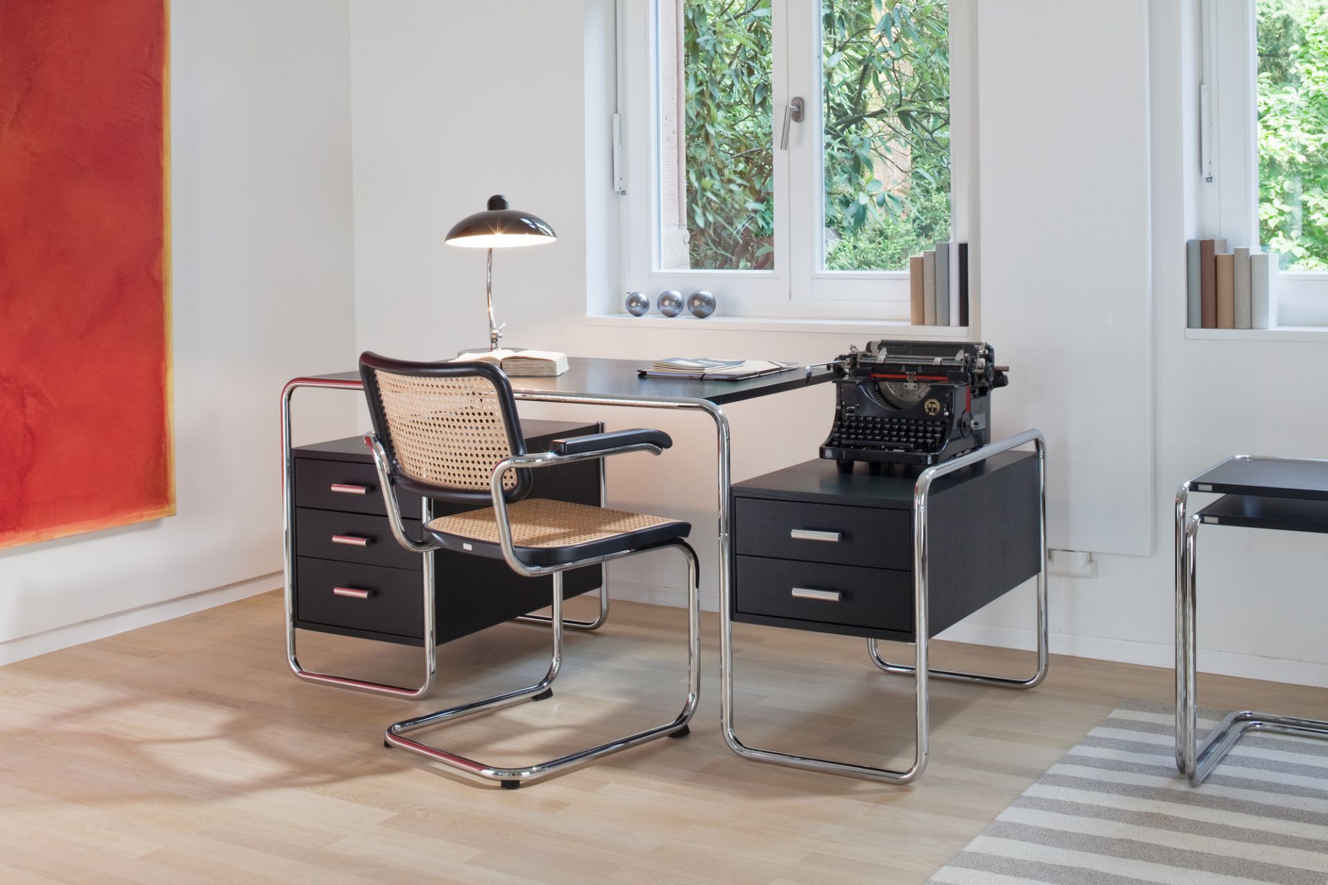 S 285 Stahlrohr Schreibtisch von Thonet mit schwarzer Tischplatte und verchromtem Stahlrohrgestell in einem hellen Raum.
