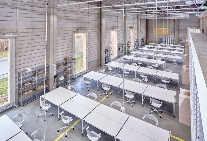 Helle Werkshalle mit Reihen von weißen Tischen und Mynt Bürodrehstühlen von Vitra, modernes Design.
