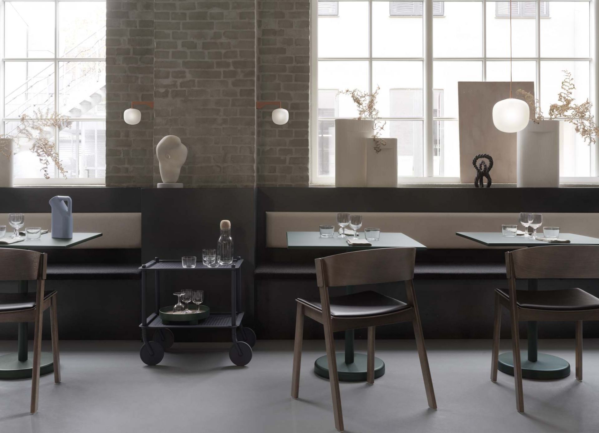 Innenaufnahme eines Restaurants mit dem Muuto Flow Trolley Servierwagen, Tischen, Stühlen und dekorativen Elementen in modernem Design.