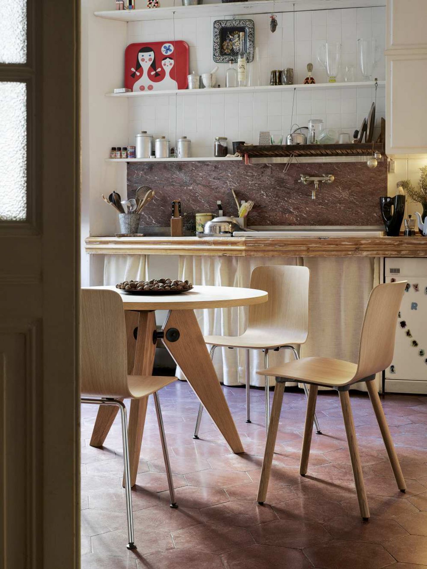 Vitra Gueridon Tisch mit drei Holzstühlen in einer Küche mit Terrakottafliesen und rustikalem Design.