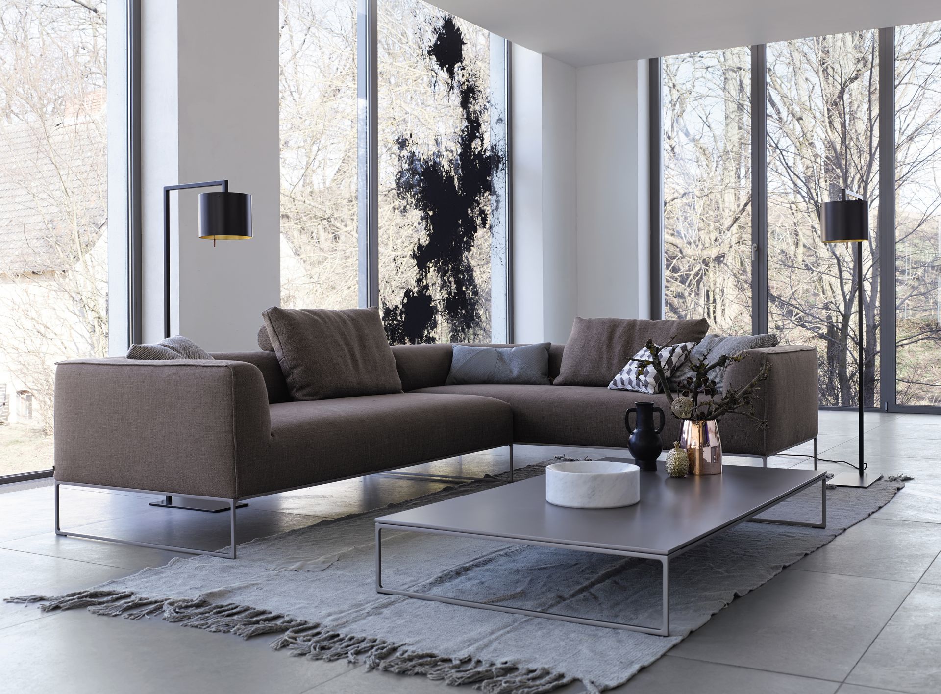 Mell Lounge Sofa in Braun mit Kissen und Couchtisch vor großen Fenstern.