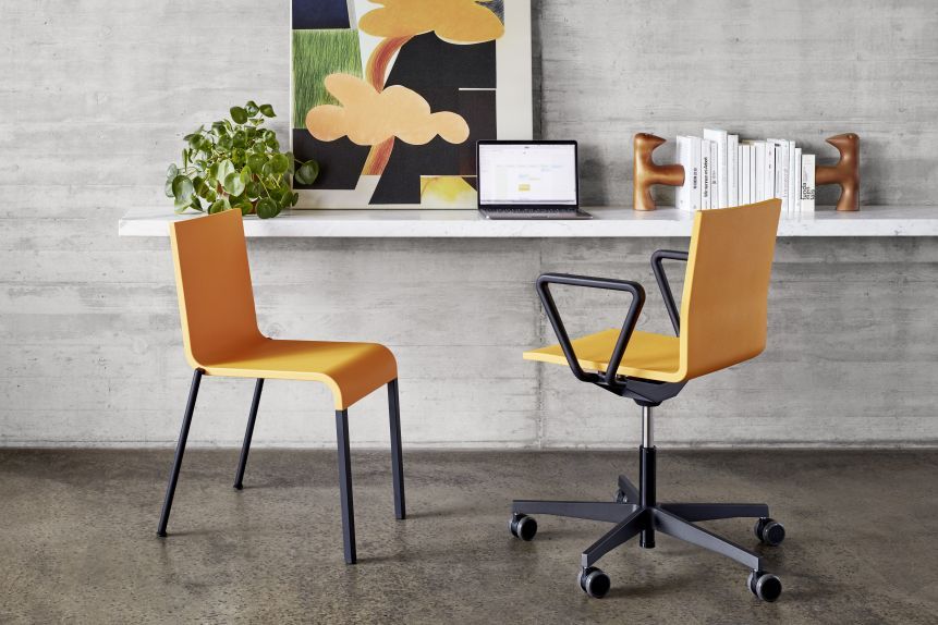 Zwei moderne Bürostühle in Gelb und Schwarz vor einer Betonwand mit Schreibtischdekoration.