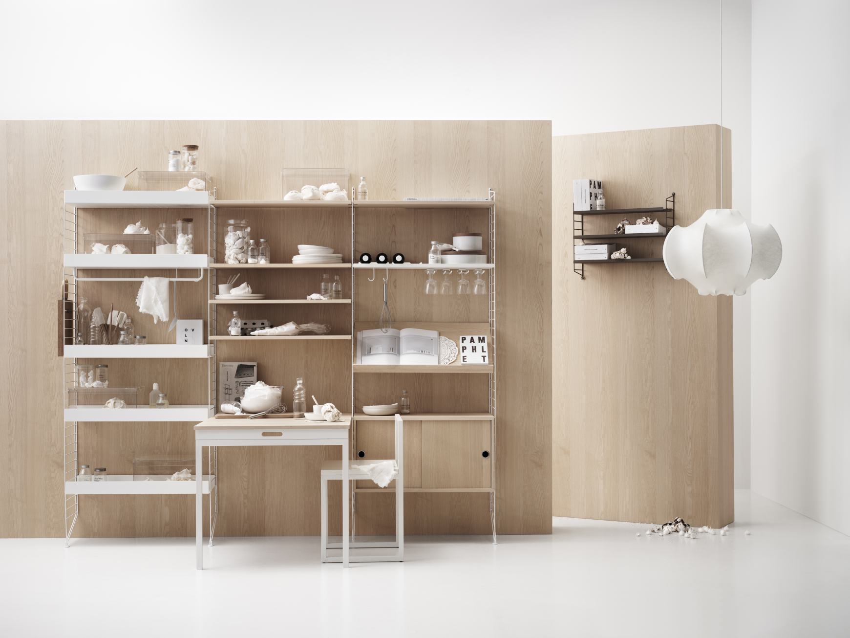 Helles Wohnzimmer mit String Furniture Regalsystem, Tisch und Stuhl, dekoriert mit Küchenutensilien und Geschirr.