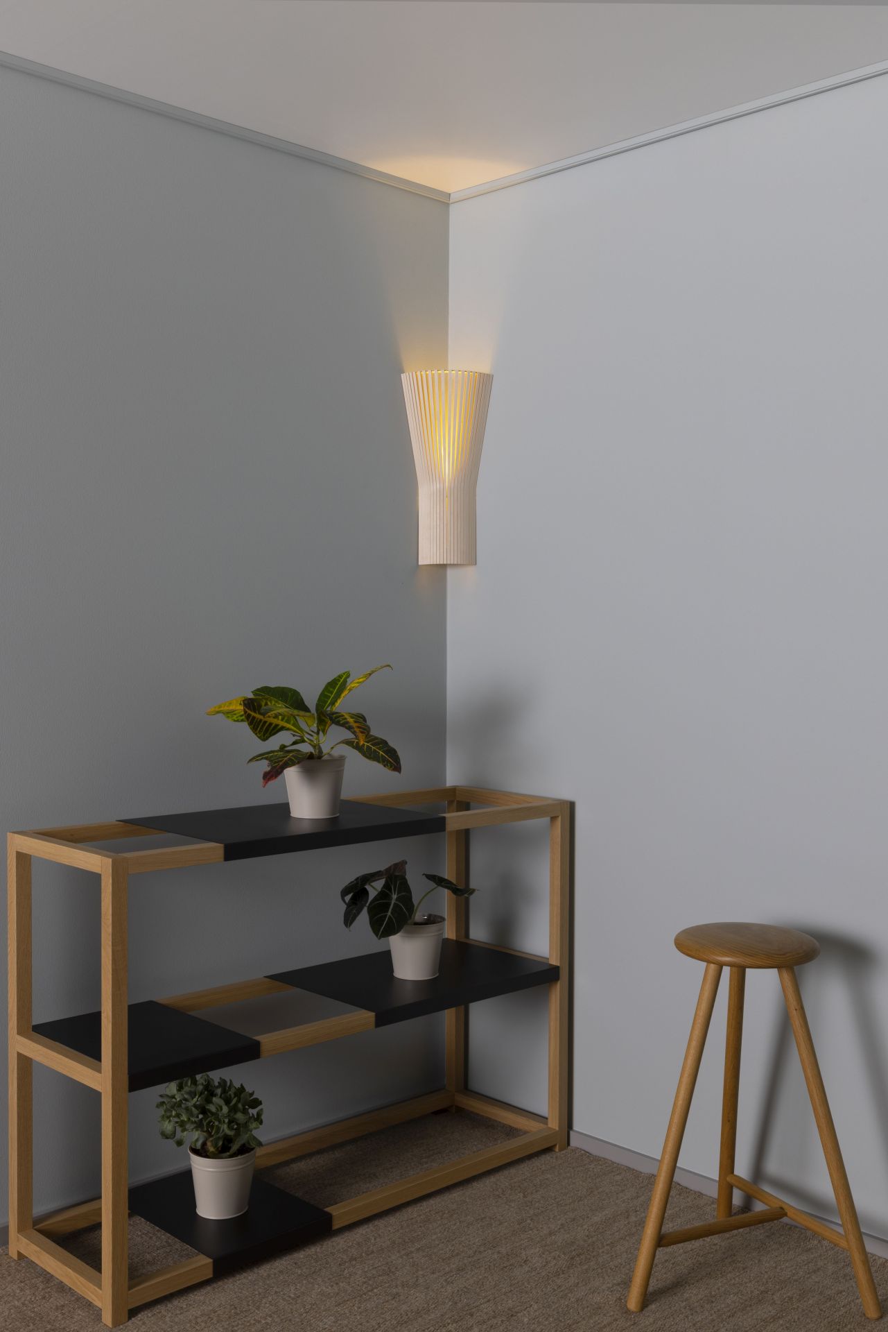 Secto Design 4237 Eckleuchte aus Birkenholz an grauer Wand, kombiniert mit Holzregal und Hocker.
