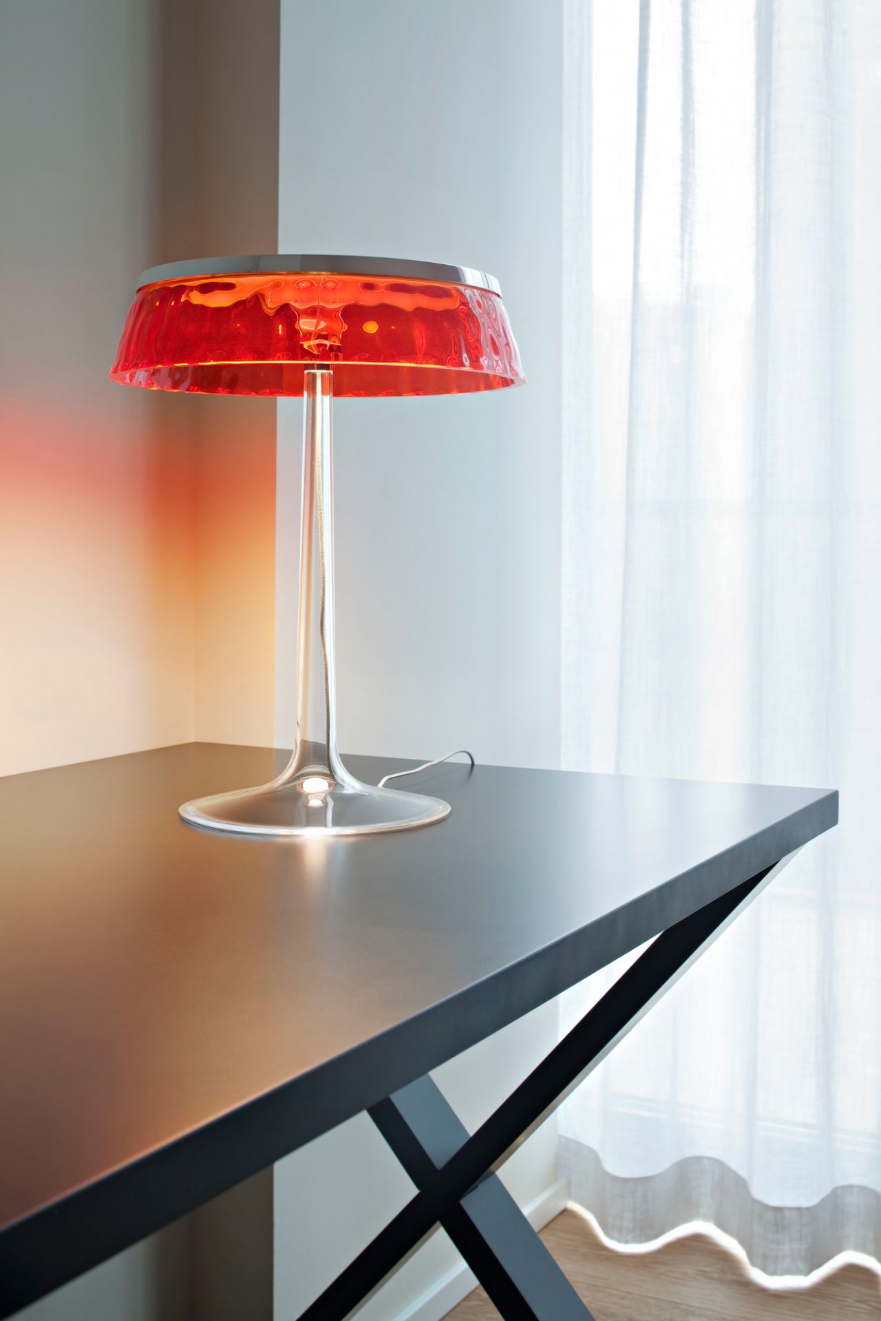 Bon Jour Tischleuchte von Flos mit rotem Schirm auf einem schwarzen Tisch. Design Lampe.