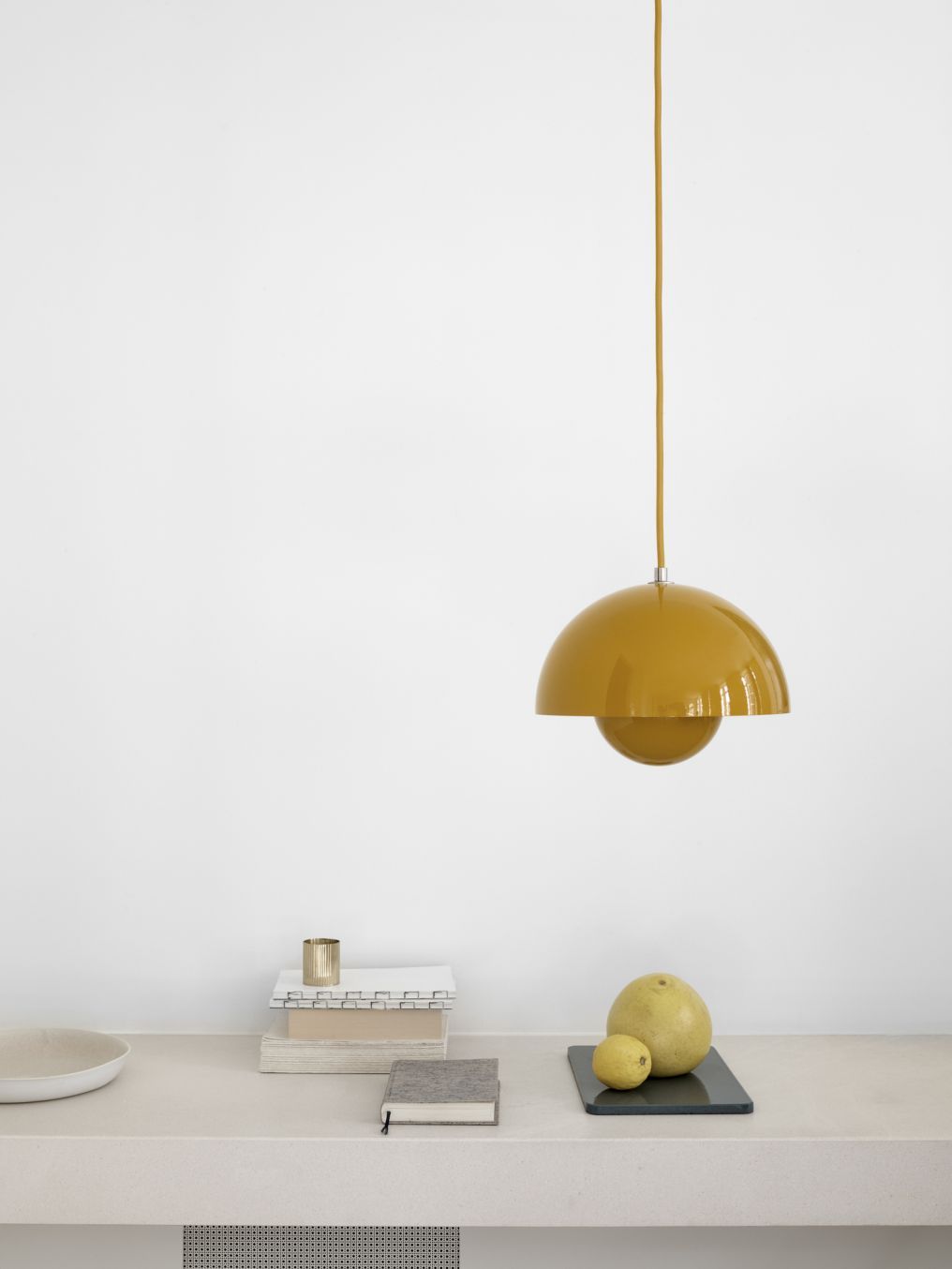 Gelbe AndTradition Flowerpot Pendelleuchte über Tisch mit Büchern und Zitrusfrüchten, modernes Design.