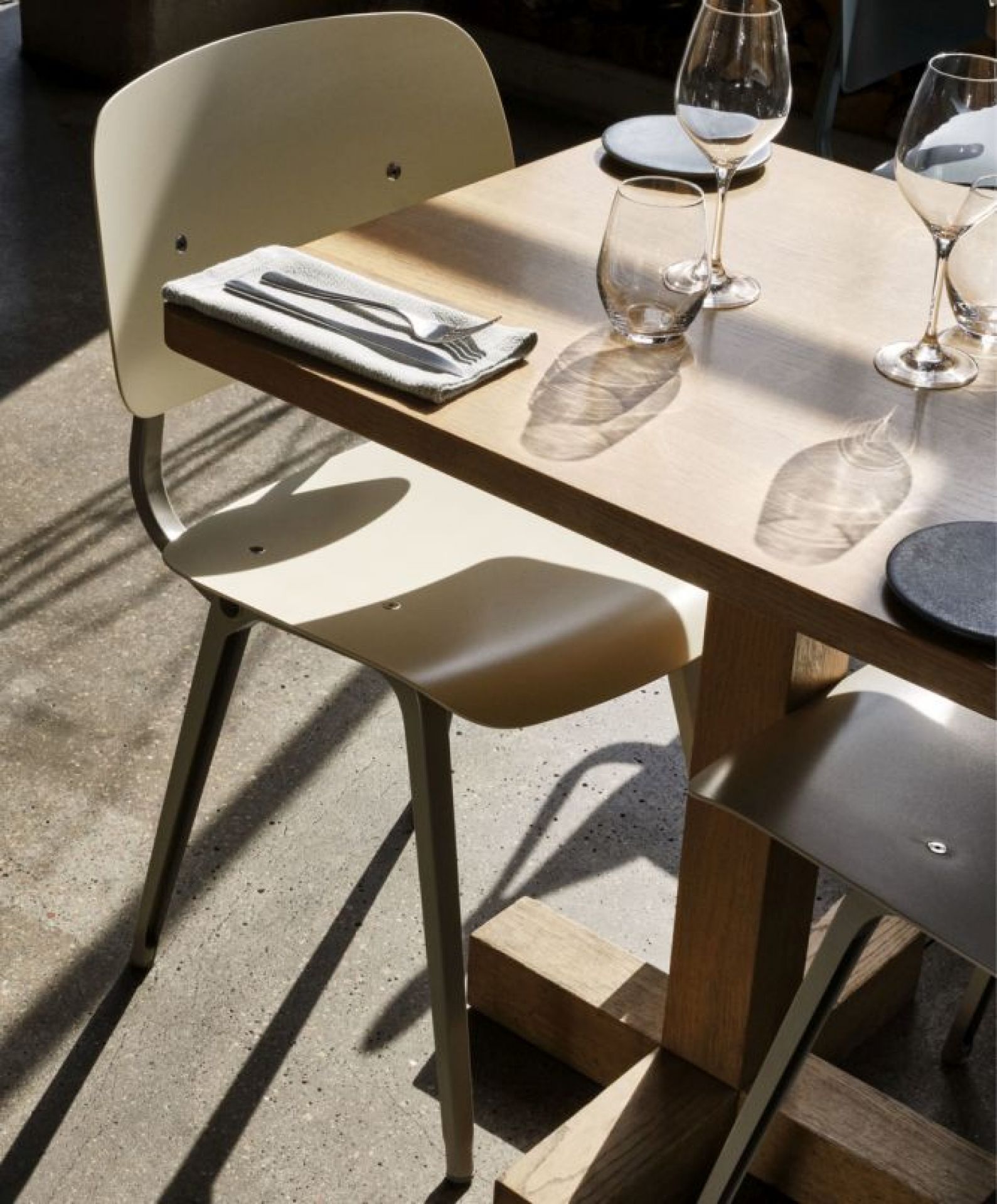 Nahaufnahme eines beigen Revolt Chair Stuhls von Hay an einem Holztisch mit Gläsern und Besteck.