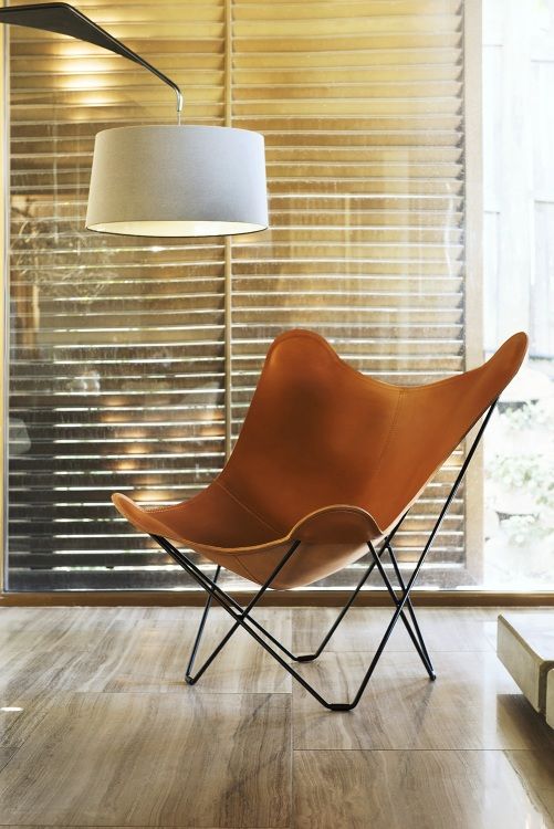 Pampa Mariposa Butterfly Chair Sessel aus braunem Leder mit schwarzem Metallgestell vor Fenster.