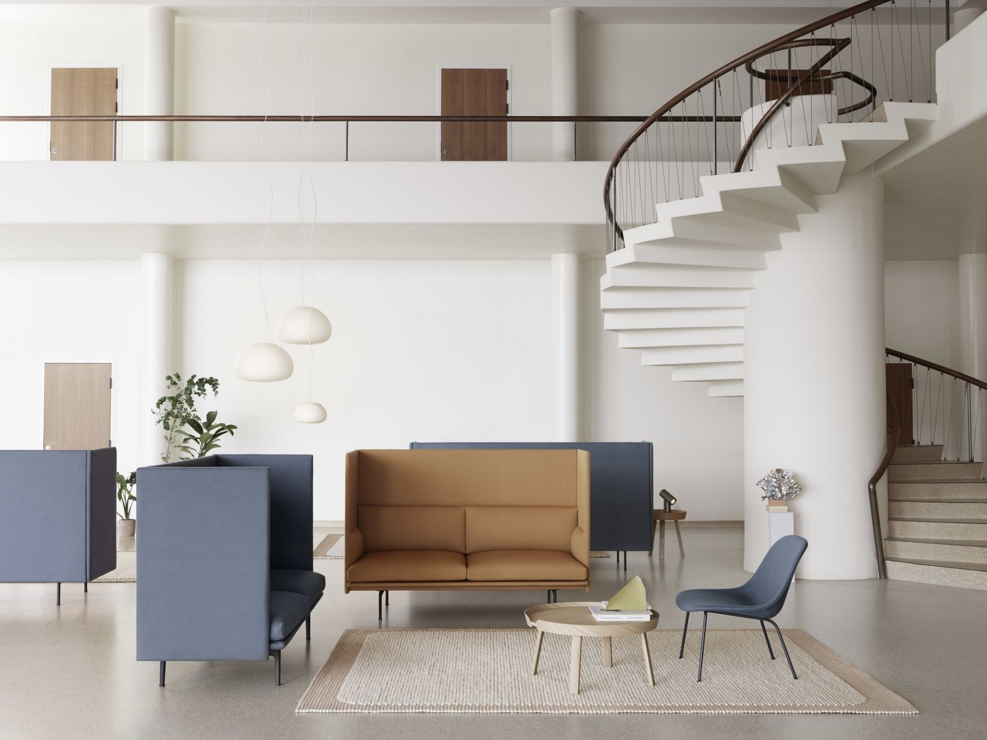 Helle, moderne Büro-Lounge mit Muuto Fluid Pendelleuchten, Sofas und Treppe im Hintergrund.