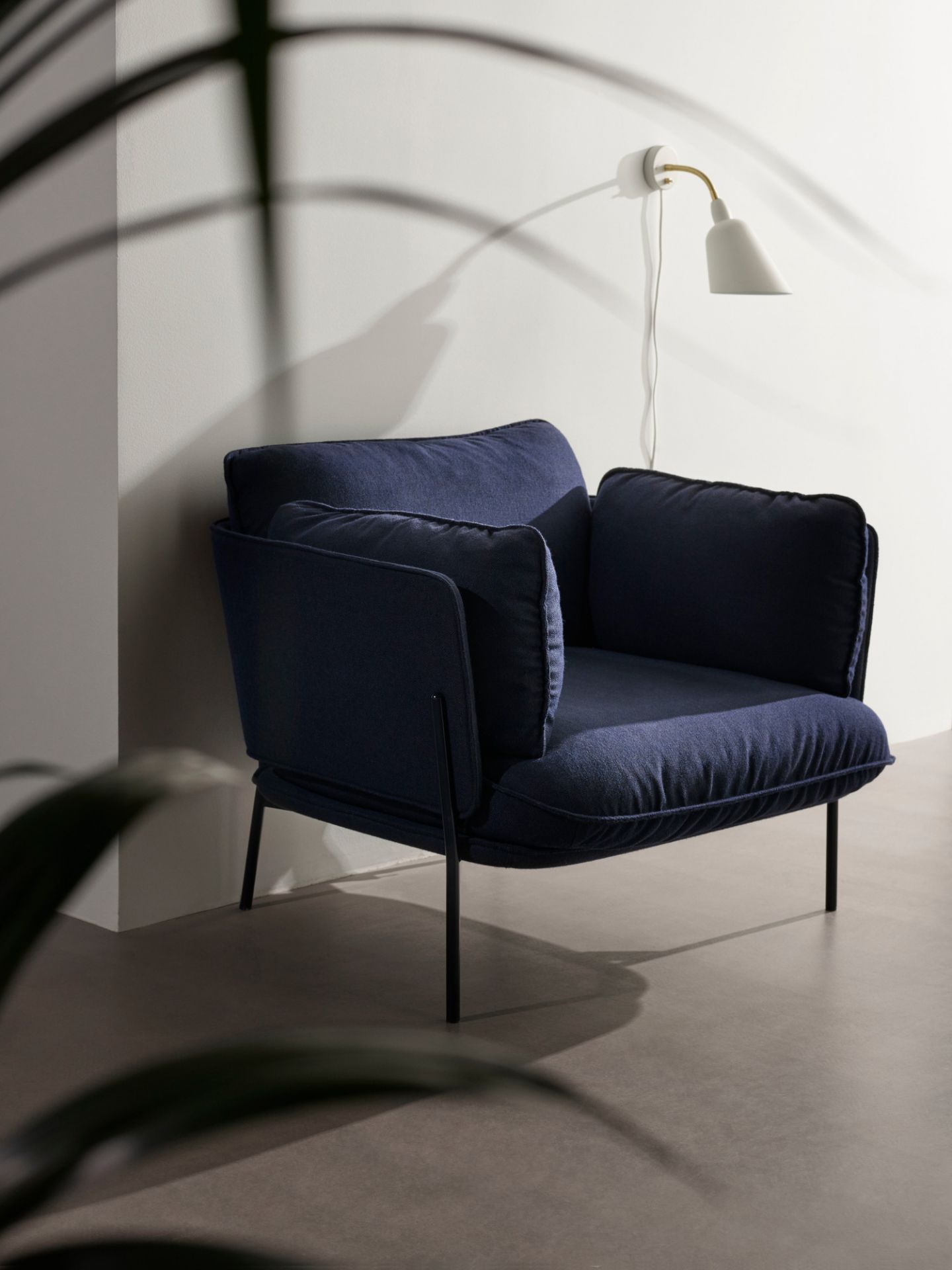 AndTradition Cloud Sessel LN1 in Dunkelblau mit Stahlgestell und passenden Kissen vor einer Wand.