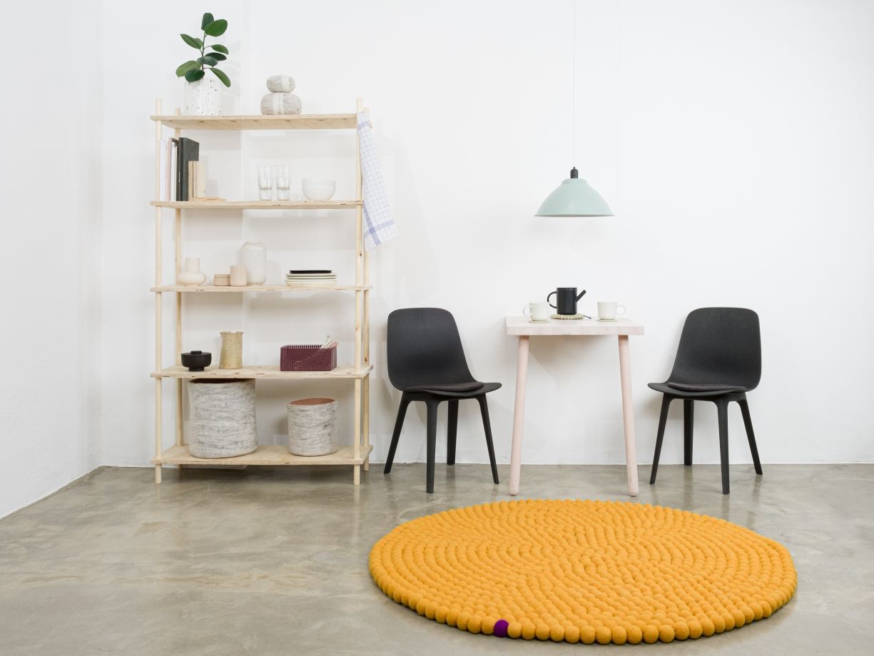 Ockergelber, runder Filzteppich von myfelt (Ø 200 cm) im minimalistischen Wohnraum mit Tisch und Stühlen.