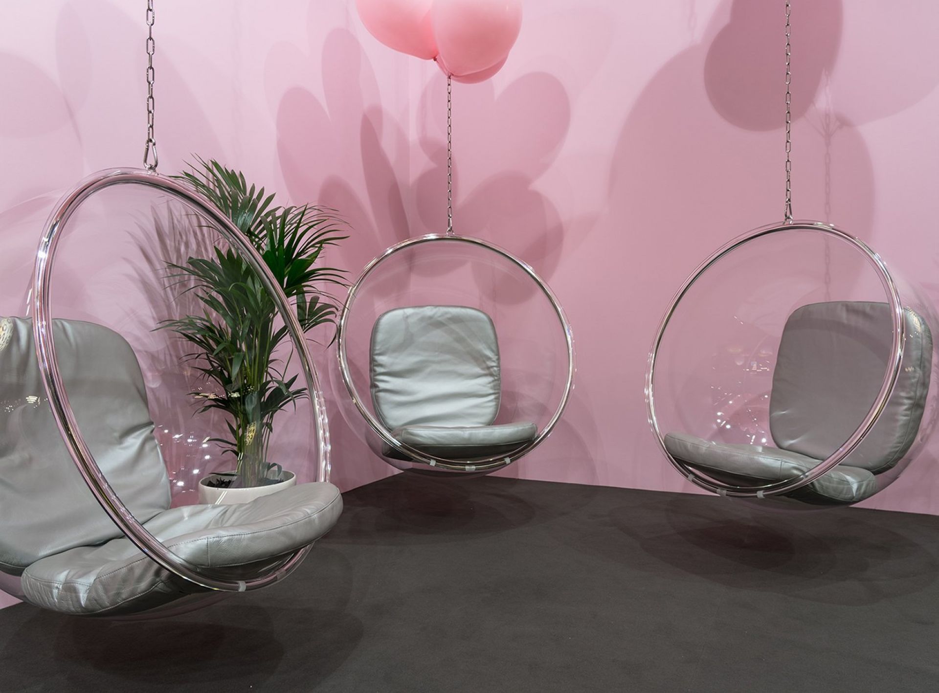Drei transparente Bubble Hängesessel von Eero Aarnio mit grauen Kissen vor rosa Wand.