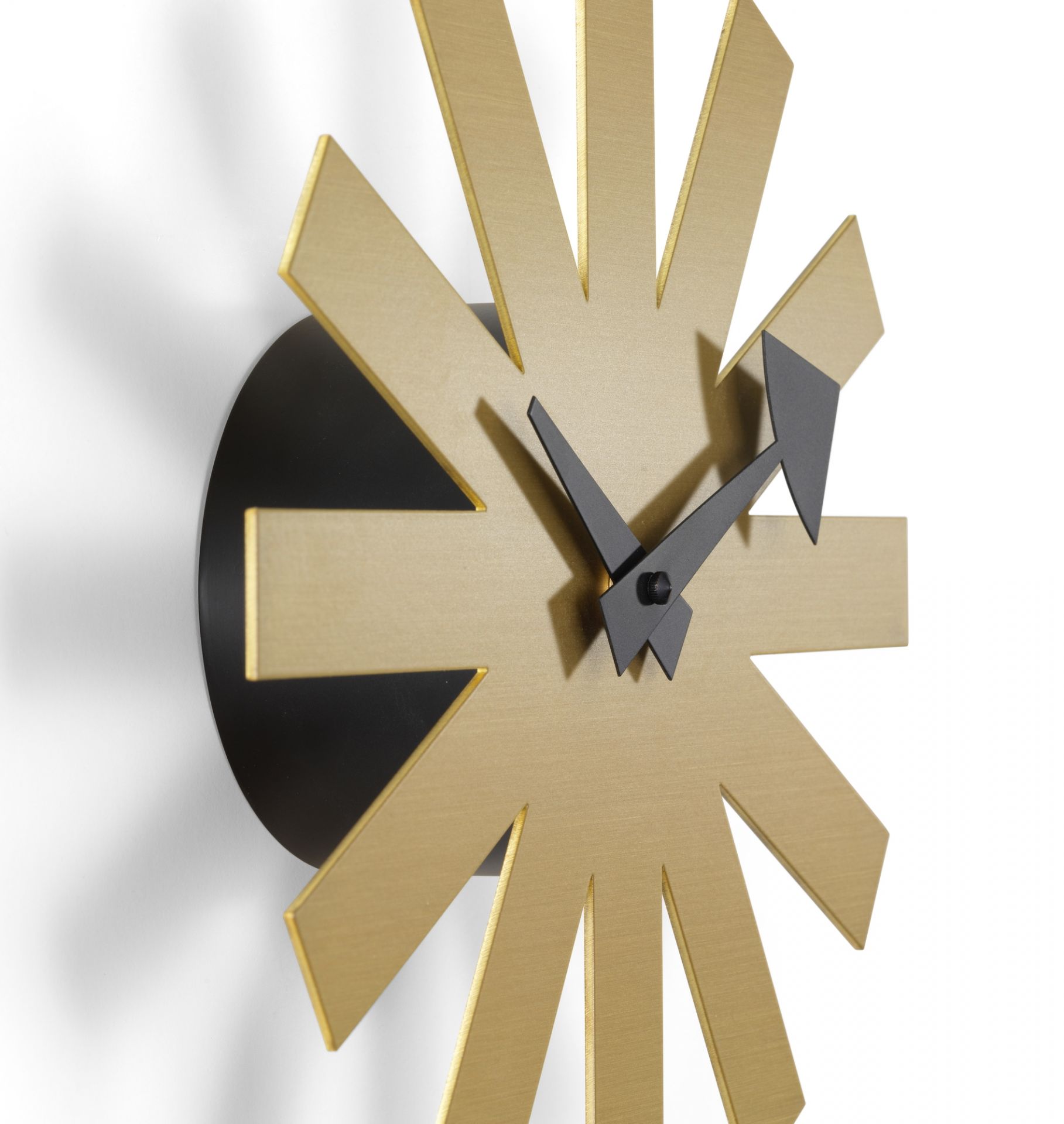 Nahaufnahme der Asterisk Wanduhr von Vitra in Messing mit schwarzen Zeigern.