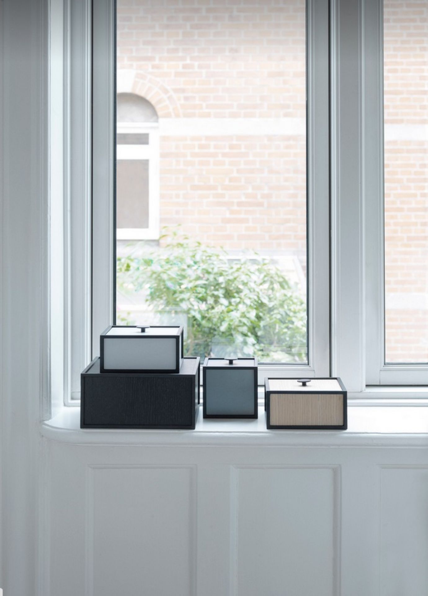 Audo Frame Aufbewahrungsboxen in verschiedenen Farben und Größen auf einer Fensterbank, stilvolle Wohnraumorganisation.