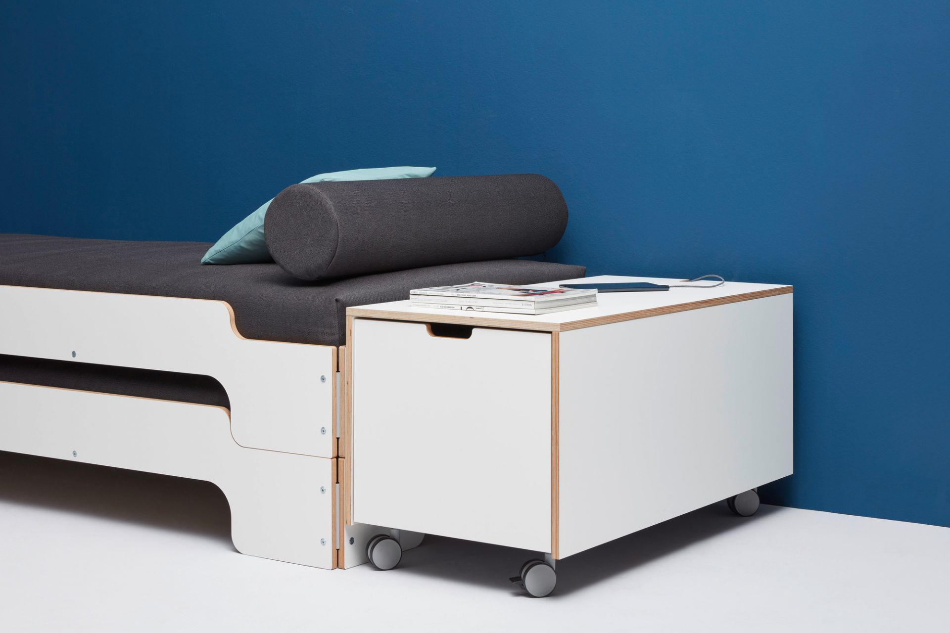 Komfort Bettkasten 16 von Müller Möbelwerkstätten mit Schubkasten auf Rollen neben einem Bett.