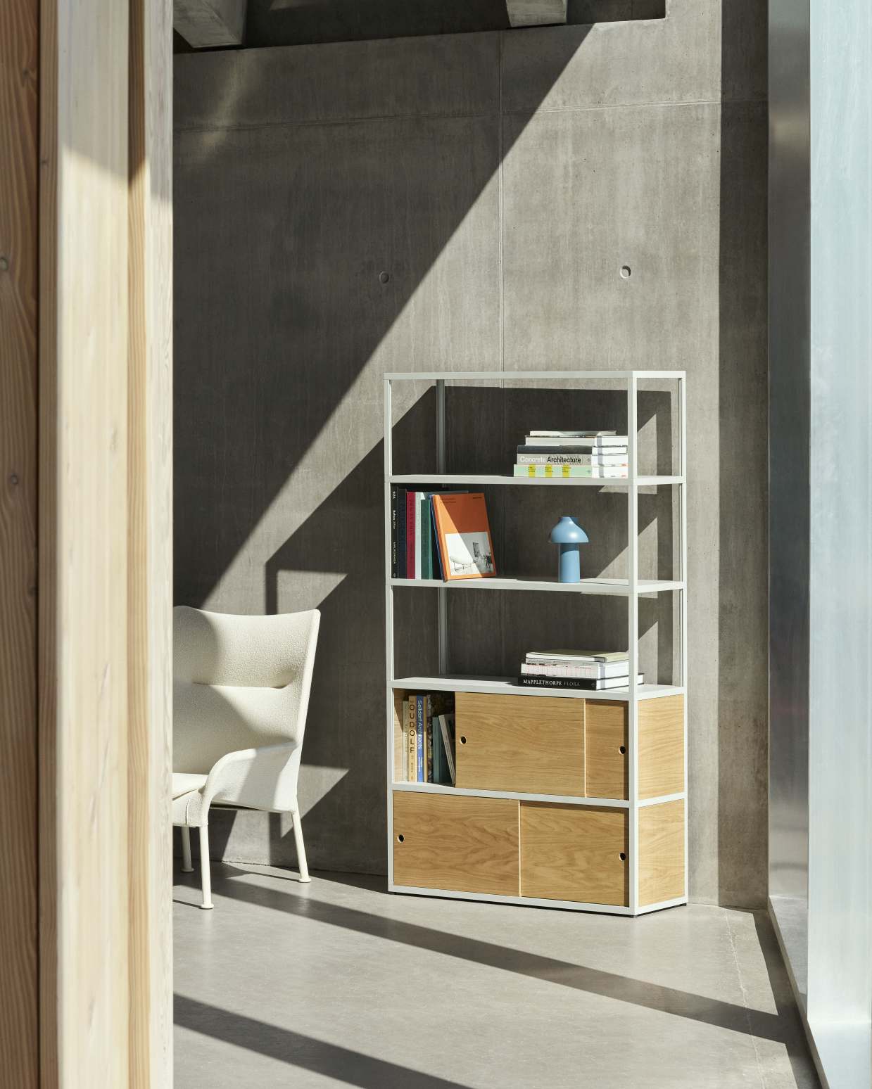 Heller 02 Lounge Chair Sessel von Hay neben einem weißen Bücherregal mit Holzschränken.