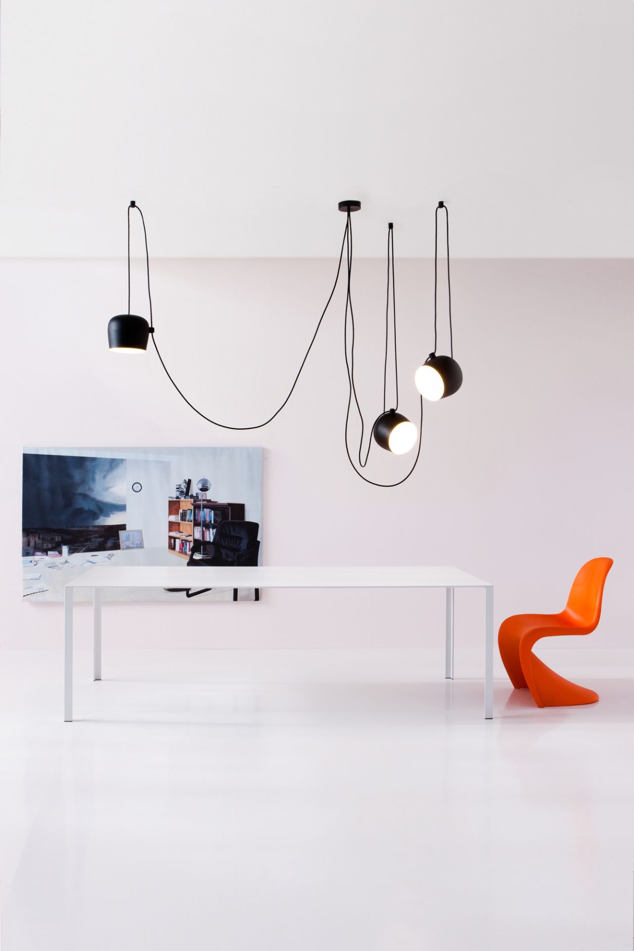Flos Aim Pendelleuchte: Schwarze LED-Hängelampe über weißem Tisch und orangefarbenem Stuhl im minimalistischen Raum.