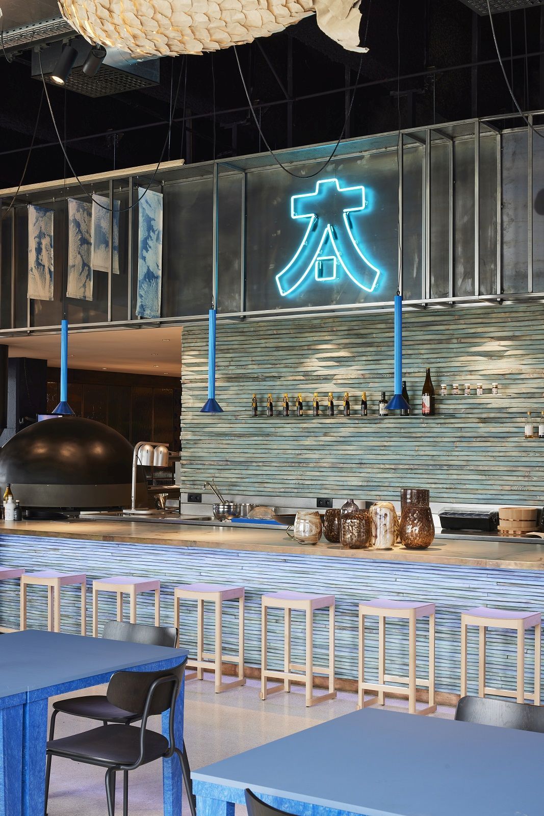 Innenaufnahme eines Restaurants mit Atelier Barhockern von Artek an einer Bar mit Neonzeichen.