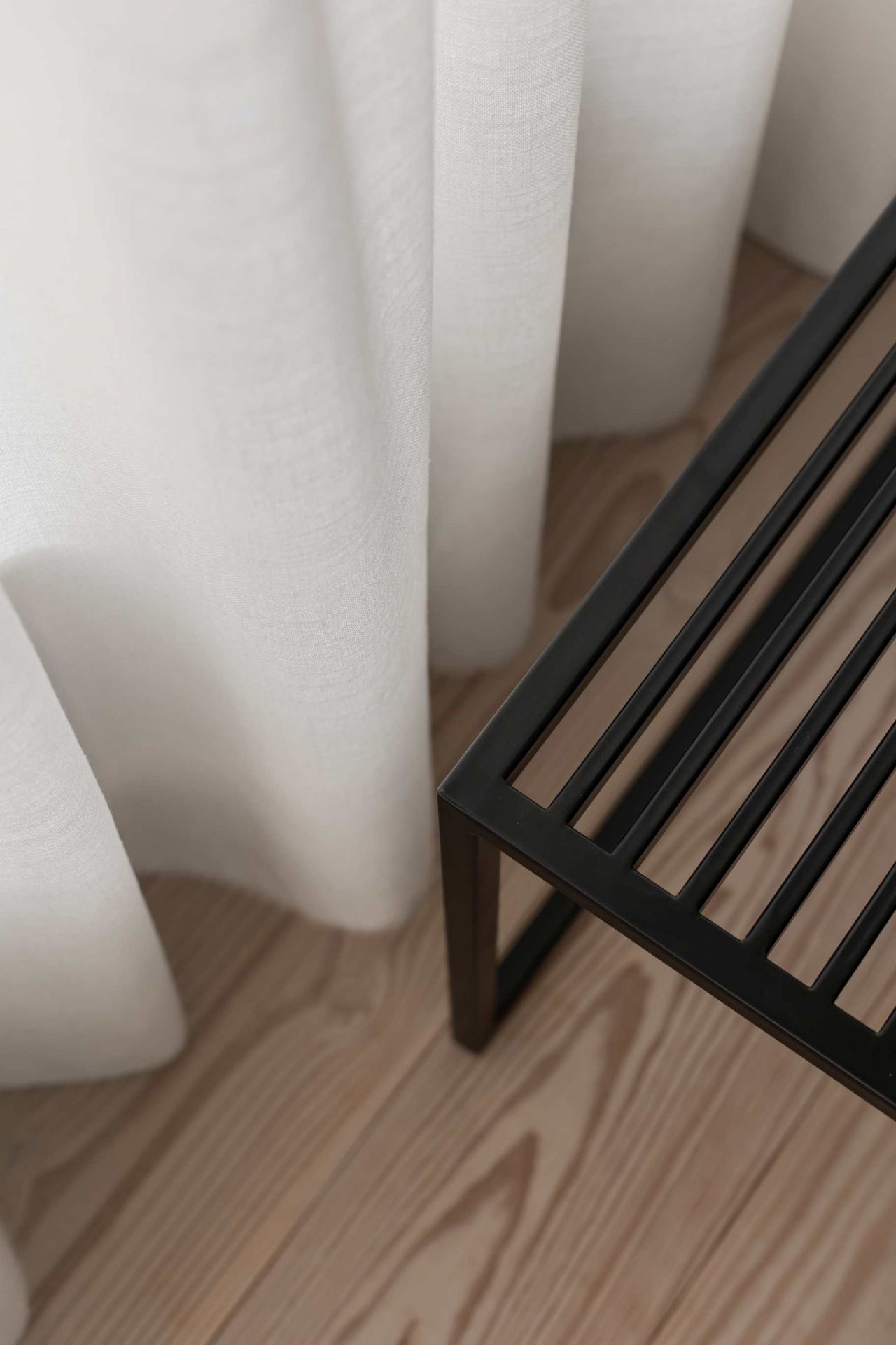Novoform Element Bank in Schwarz, minimalistisches Design mit Holzfußboden und weißem Vorhang im Hintergrund.