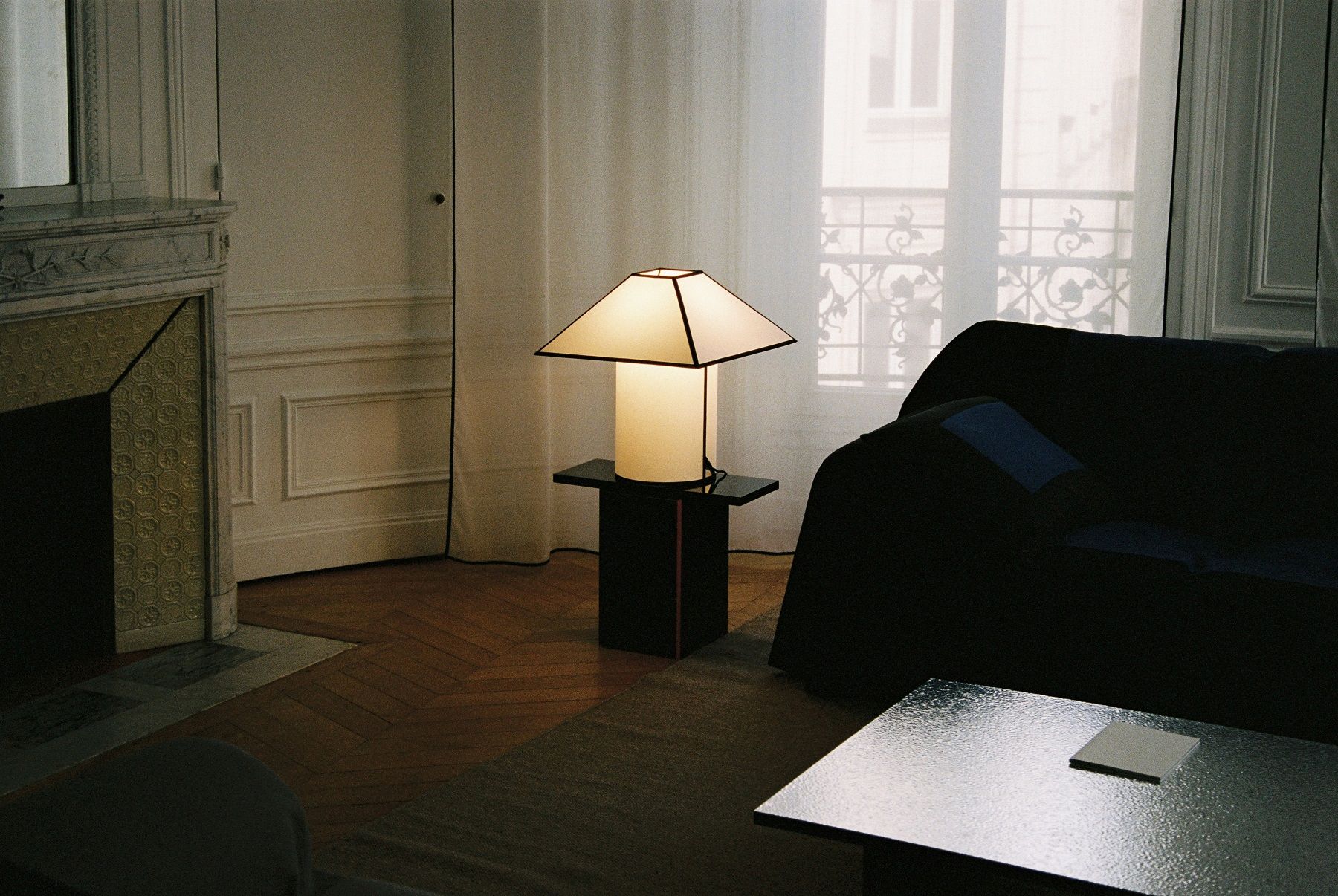 Ava Pyramid Table Lamp von Hay auf Nachttisch im Wohnzimmer mit Kamin und Sofa.