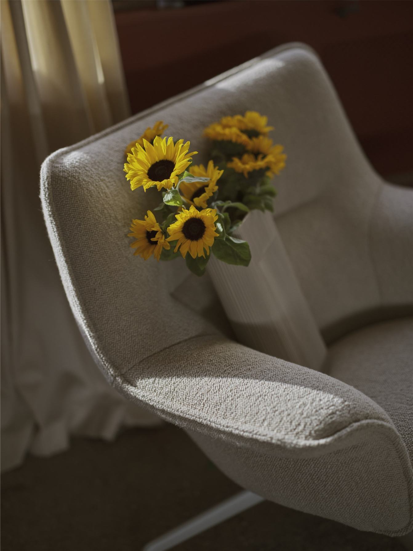 Nahaufnahme des Muuto Doze Lounge Sessels in Beige mit Sonnenblumen in einer Vase.