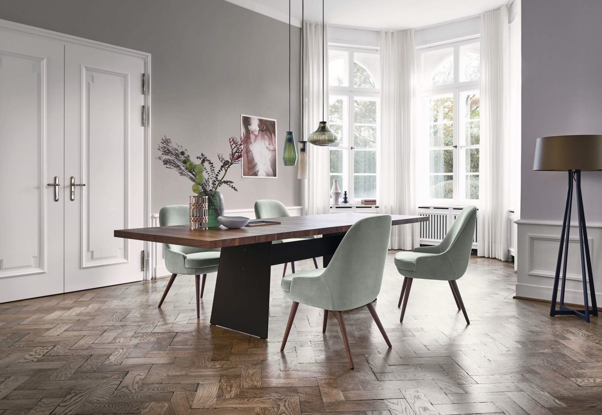 Esszimmer mit Walter Knoll Tadeo Tisch aus dunklem Holz und hellgrünen Stühlen auf Parkettboden.