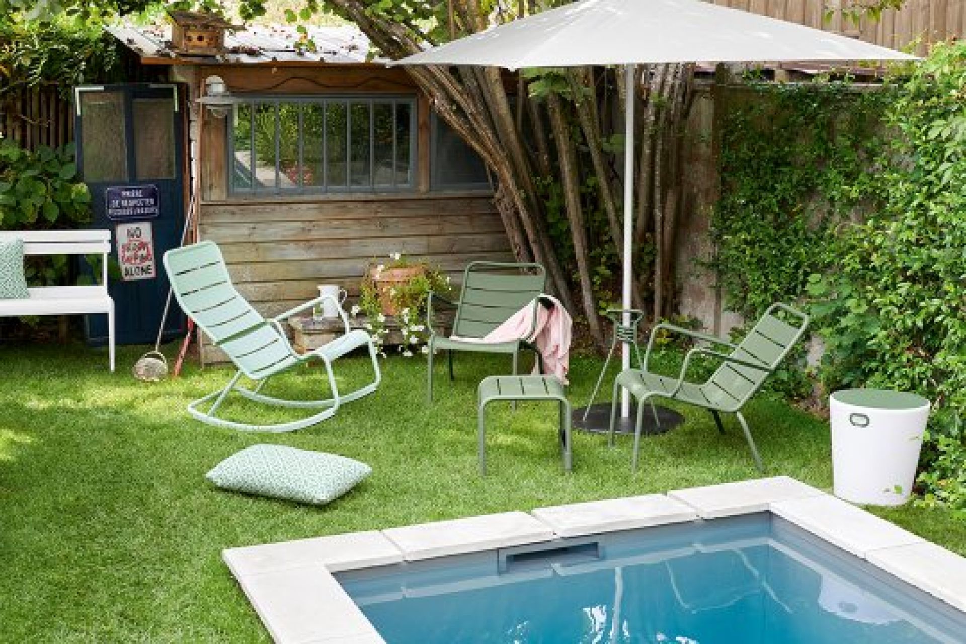 Luxembourg Outdoor Beistelltisch/Fußteil von Fermob im Garten neben Pool und weiteren Gartenmöbeln.
