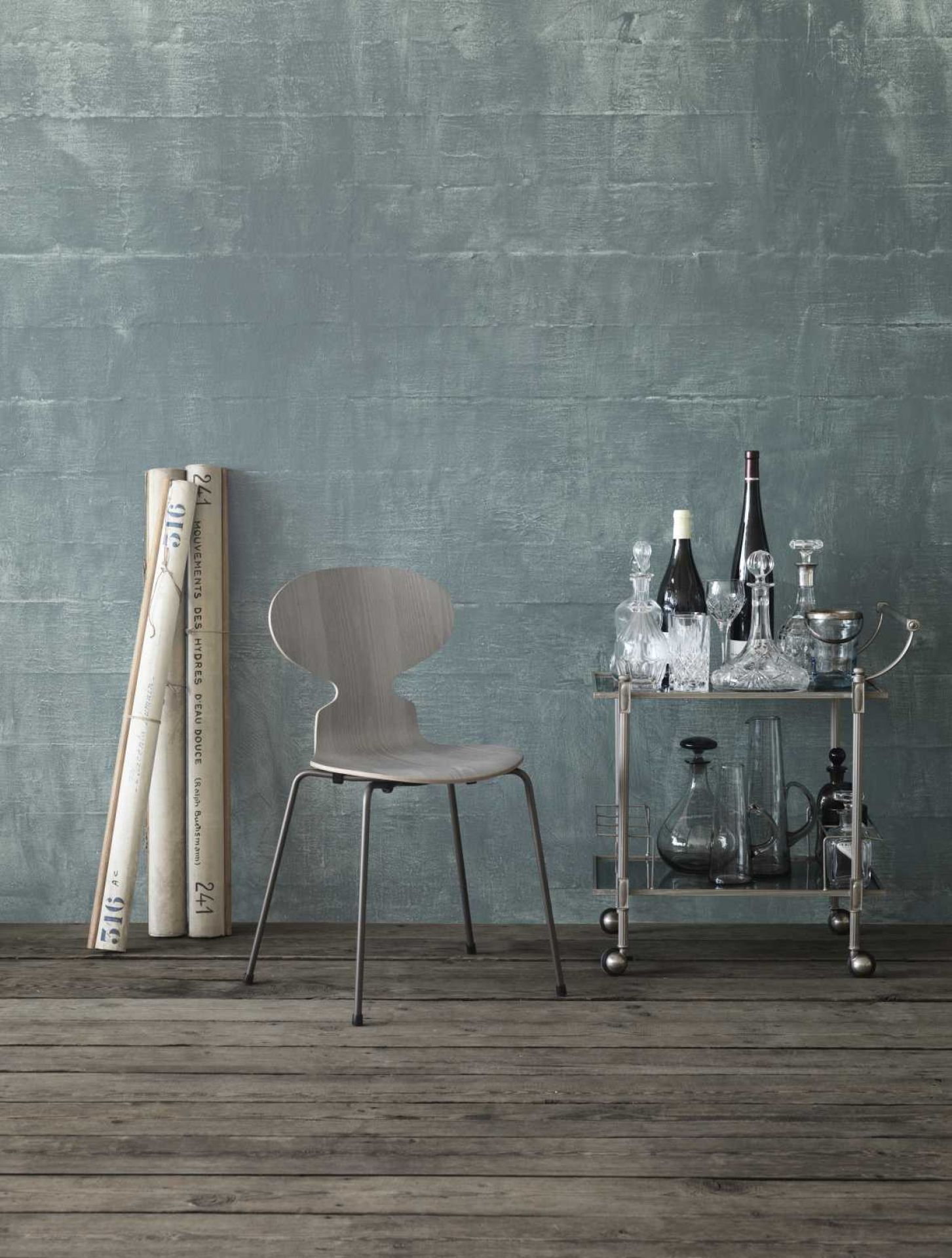 Fritz Hansen Ameise Stuhl mit vier Beinen und grauem Holzfurnier vor blauem Hintergrund.