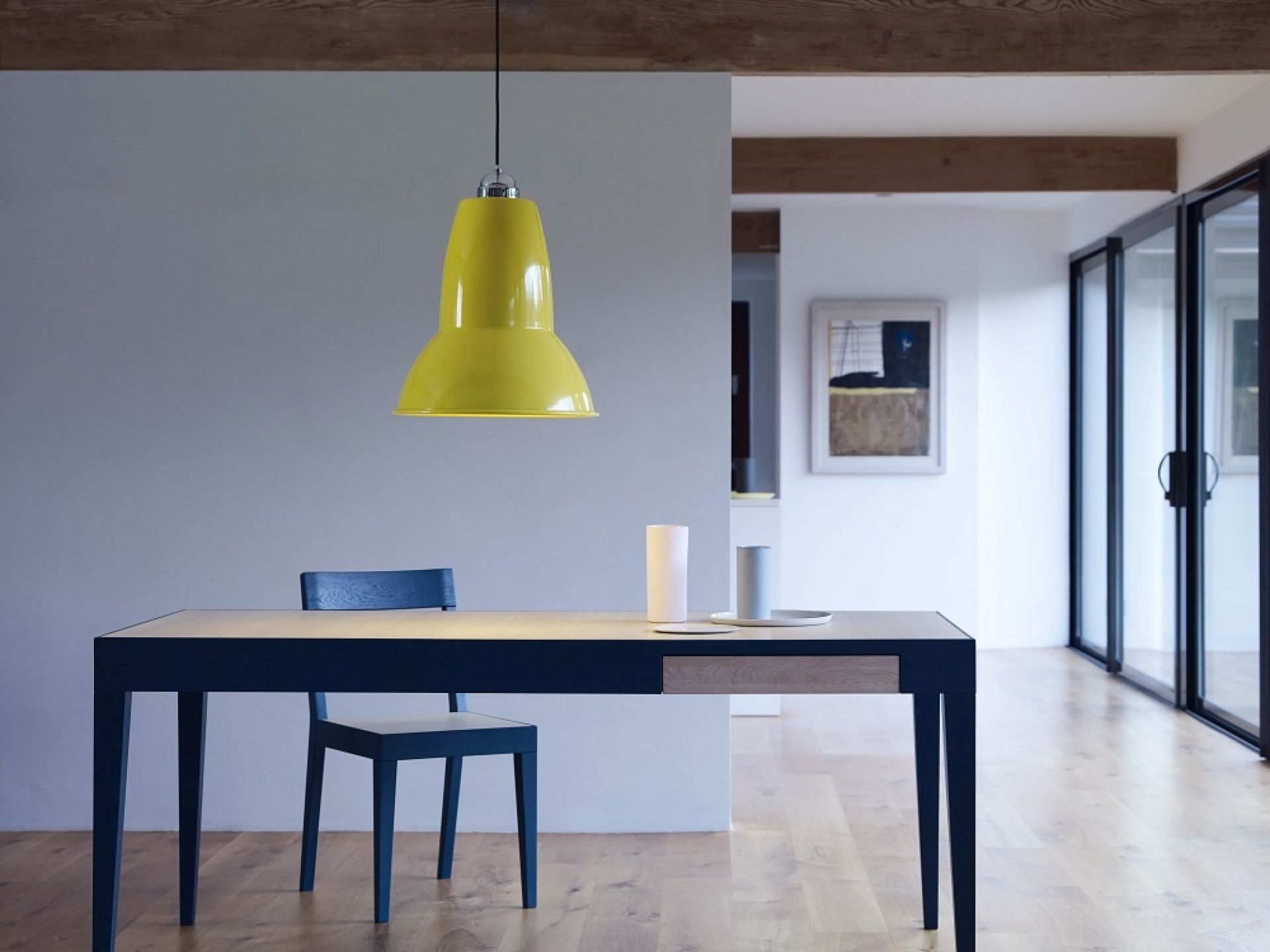 Gelbe Hängelampe über Esstisch mit blauem Stuhl und minimalistischer Dekoration in modernem Interieur.