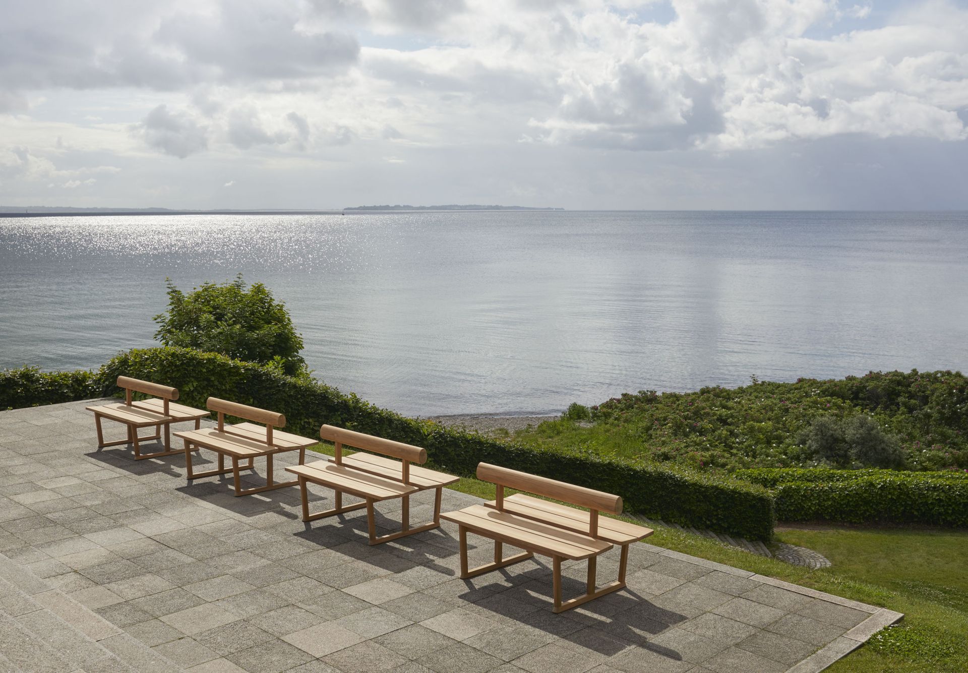 Reihe von Banco Teak Bänken von Skagerak im Außenbereich mit Meerblick. Gartenmöbel.