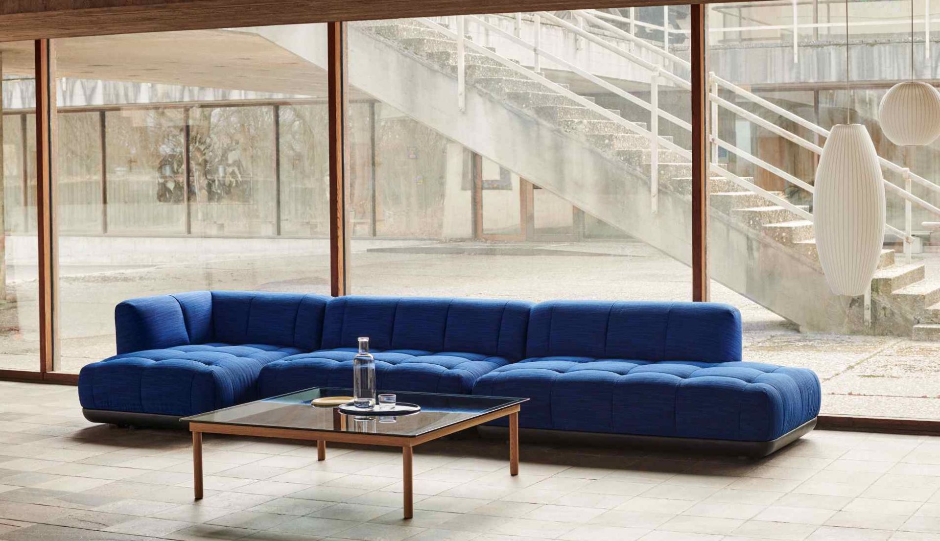 Kofi Couchtisch von Hay, quadratisch mit Glasplatte und Holzgestell vor blauem Sofa.