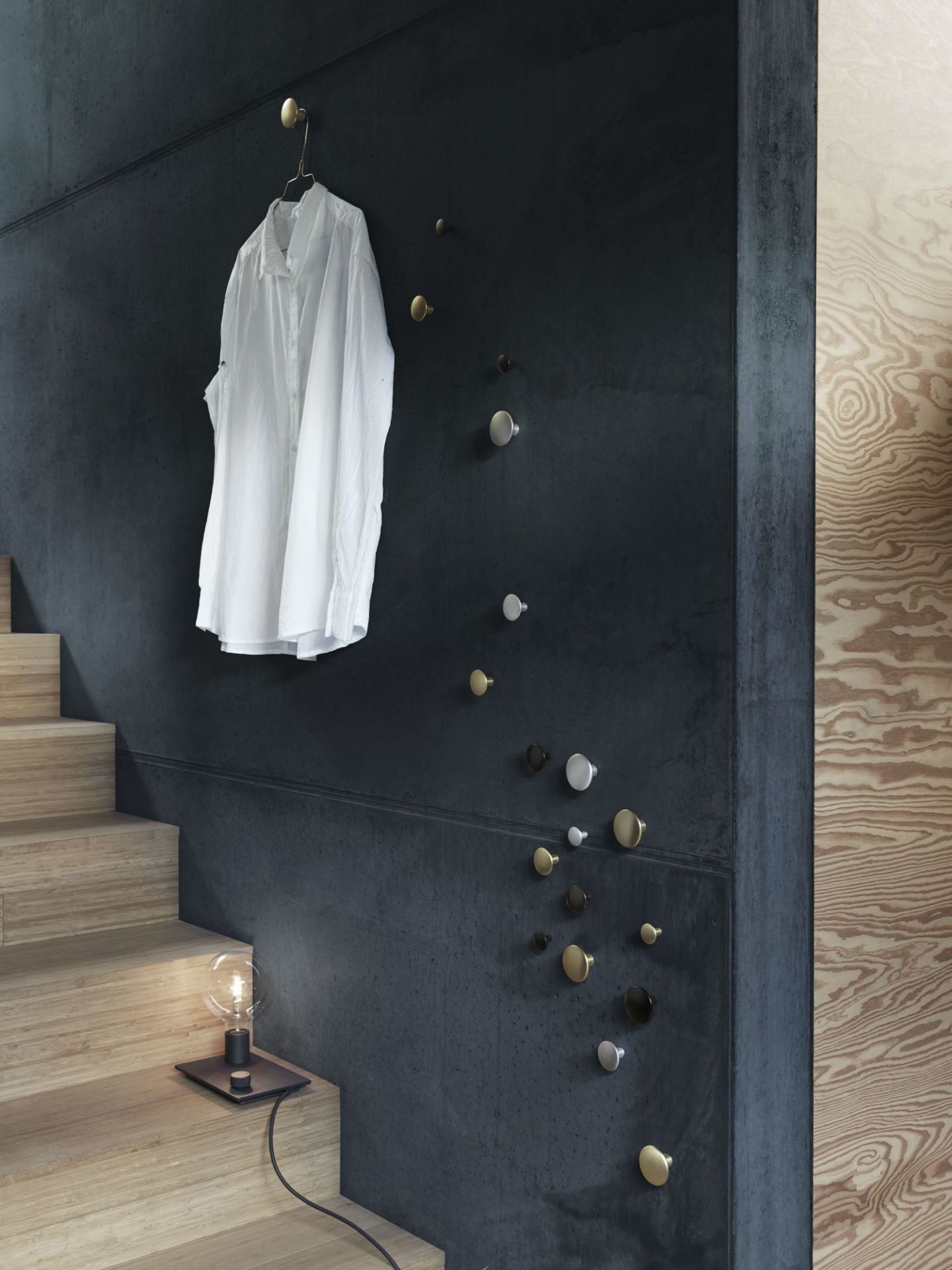 Wand mit The Dots Garderobenhaken von Muuto in Grau, Weiß, Gold und Schwarz, Treppe mit Lampe.