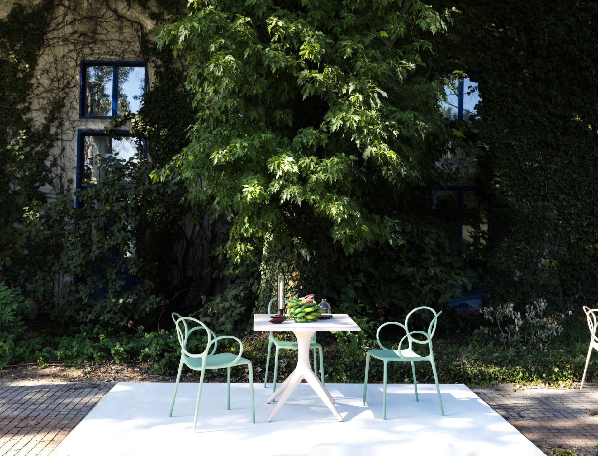Driade Sissi Armlehnstuhl in Mintgrün für den Garten, mit Tisch und üppigem Grün.