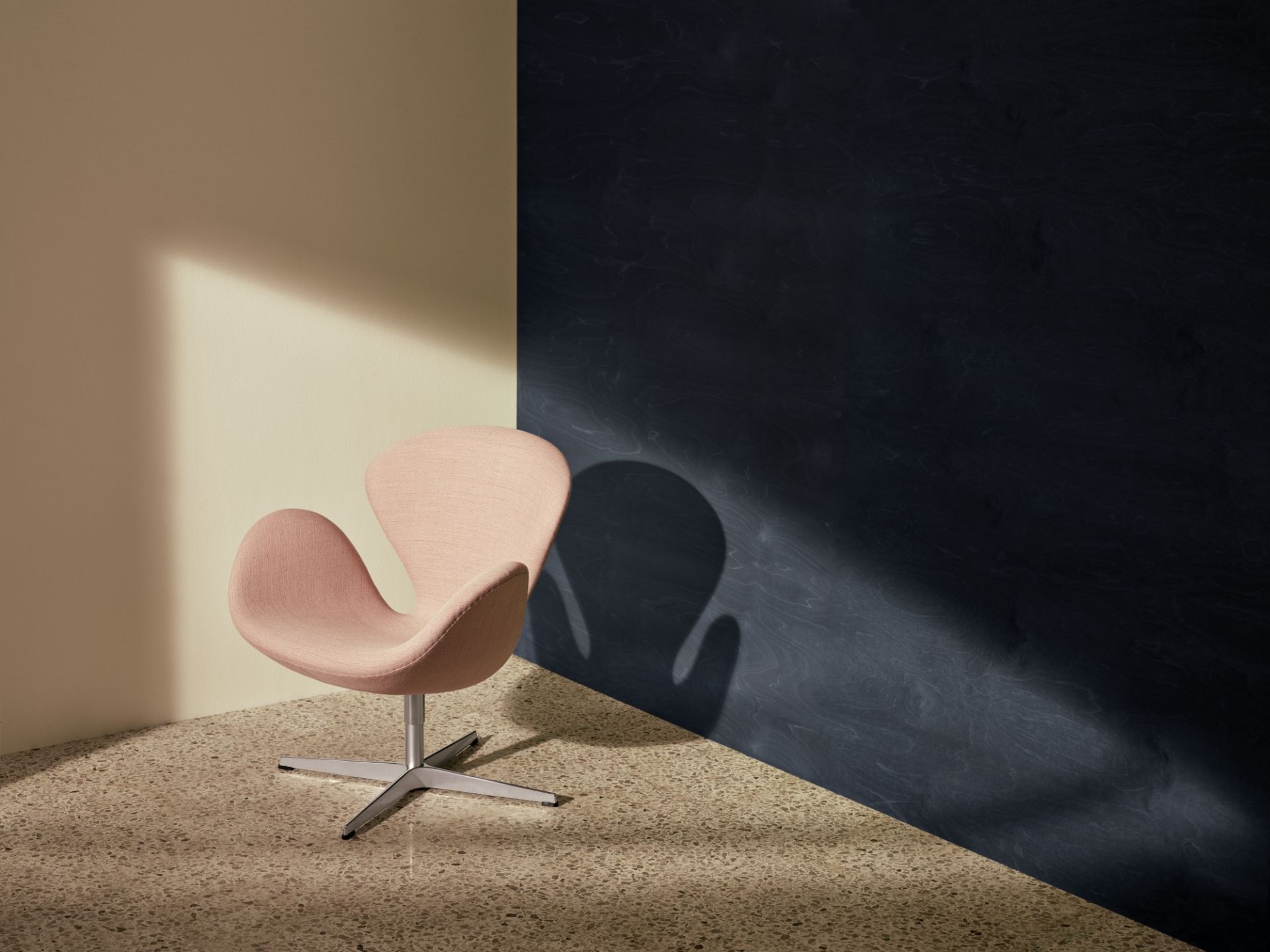 Rosa Schwan Sessel von Fritz Hansen mit Drehfuß vor beiger und dunkelblauer Wand.