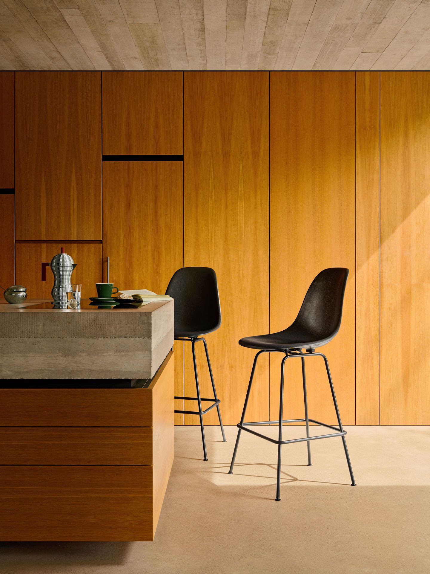 Zwei schwarze Eames Fiberglass Barhocker von Vitra mit Sitzpolster an einer Küchentheke aus Beton.