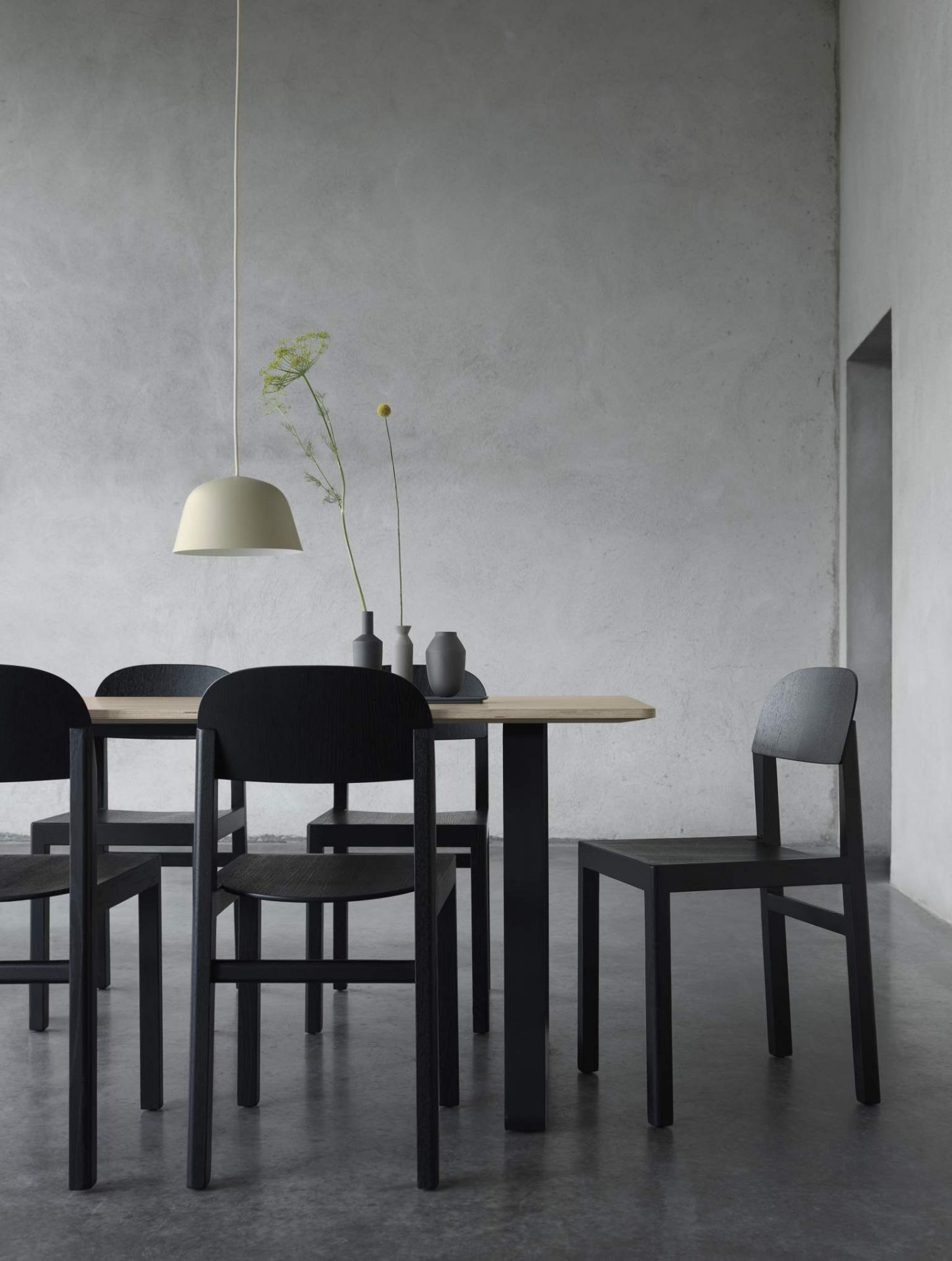 Helle Ambit Pendelleuchte von Muuto über Esstisch mit schwarzen Holzstühlen und minimalistischer Dekoration.
