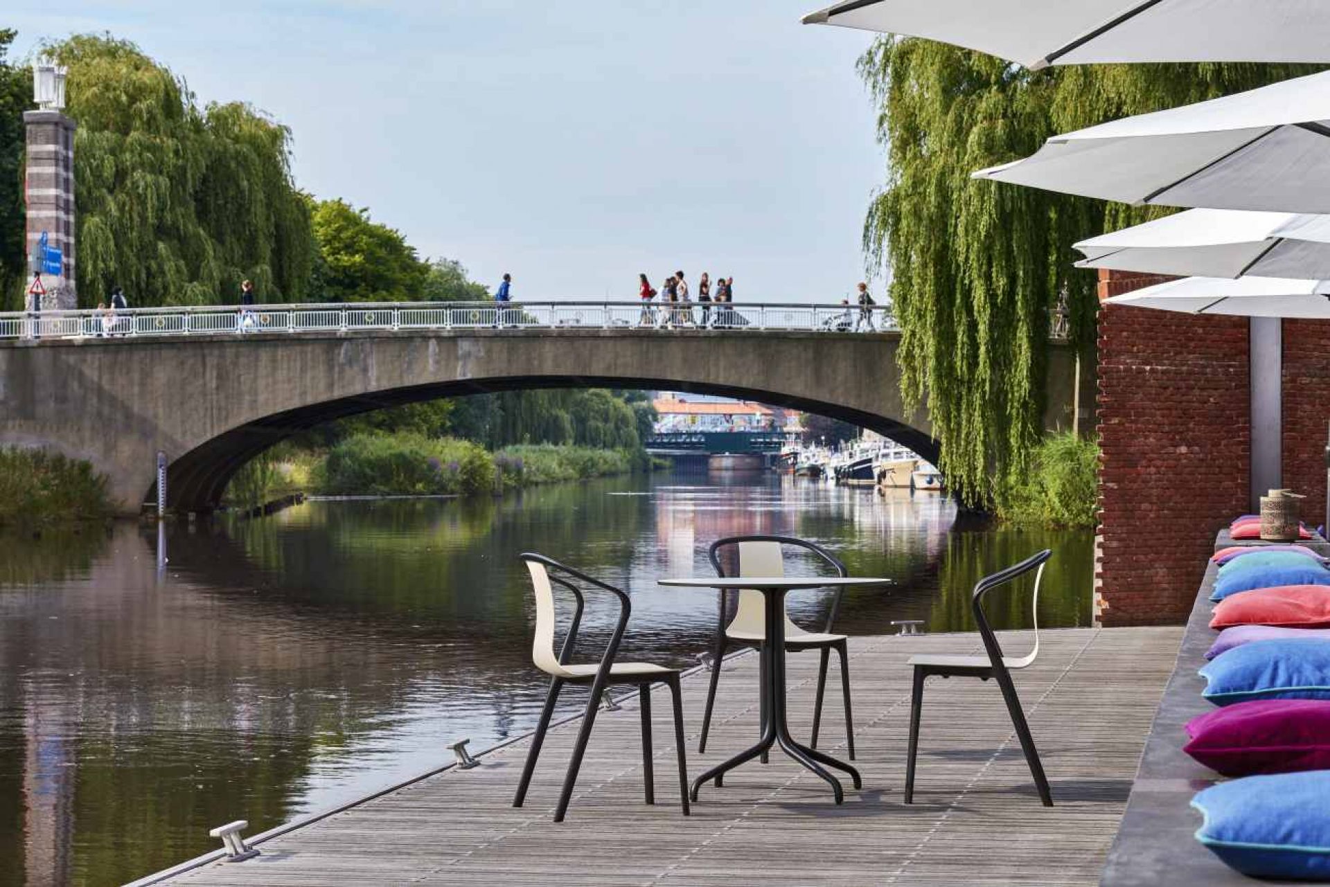 Vitra Belleville Table Tisch mit Stühlen am Flussufer unter einer Brücke, Außenbereich.