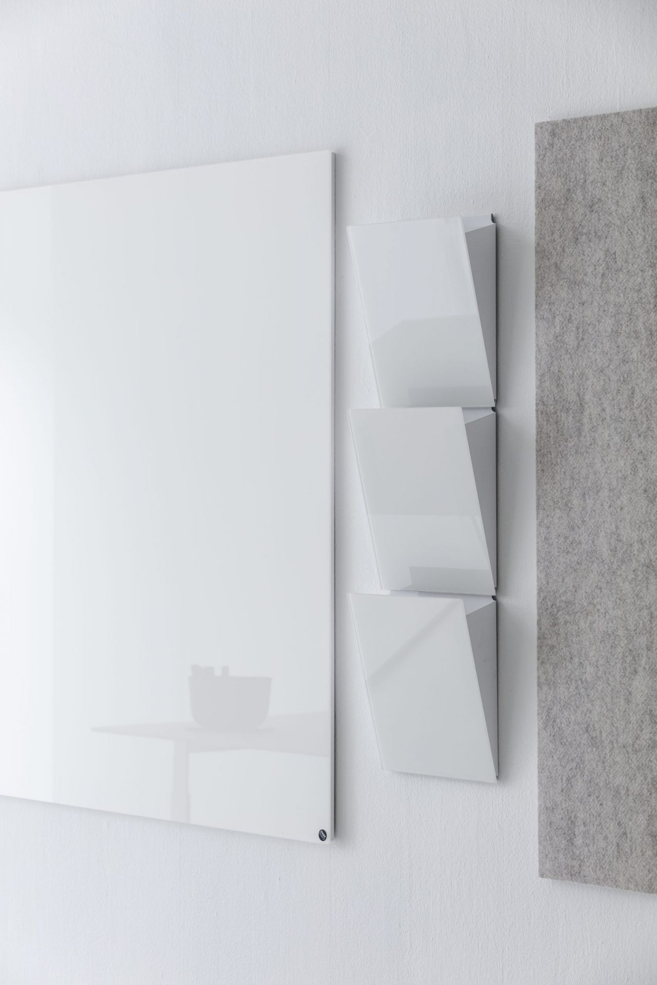 Chat Board Classic, weiße magnetische Glas-Wandtafel neben dreiteiliger, weißer Ablage und grauer Filzplatte an einer weißen Wand.