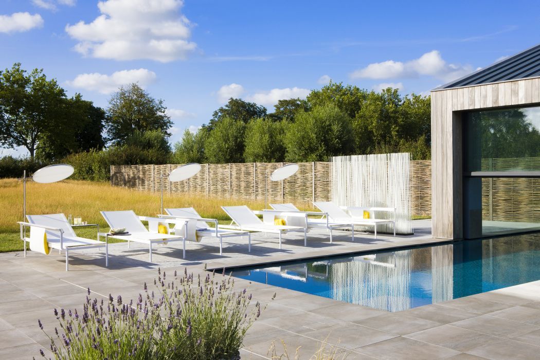 Mehrere weiße Sol + Luna Sonnenliegen von Extremis am Pool eines modernen Hauses im Freien.