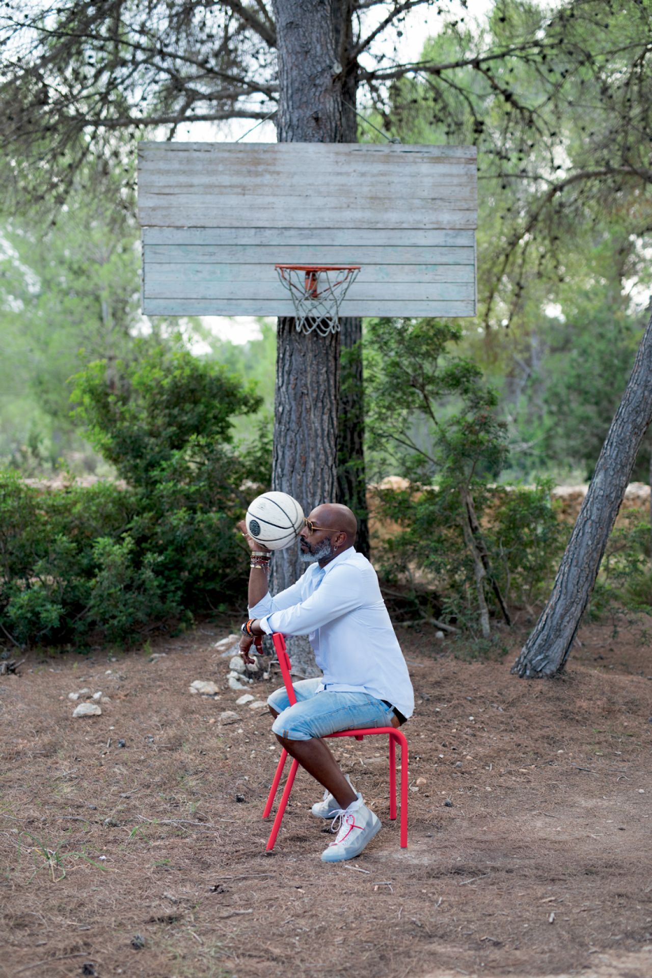 Mann sitzt auf rotem Luxembourg Outdoor Stuhl von Fermob unter Basketballkorb im Freien.
