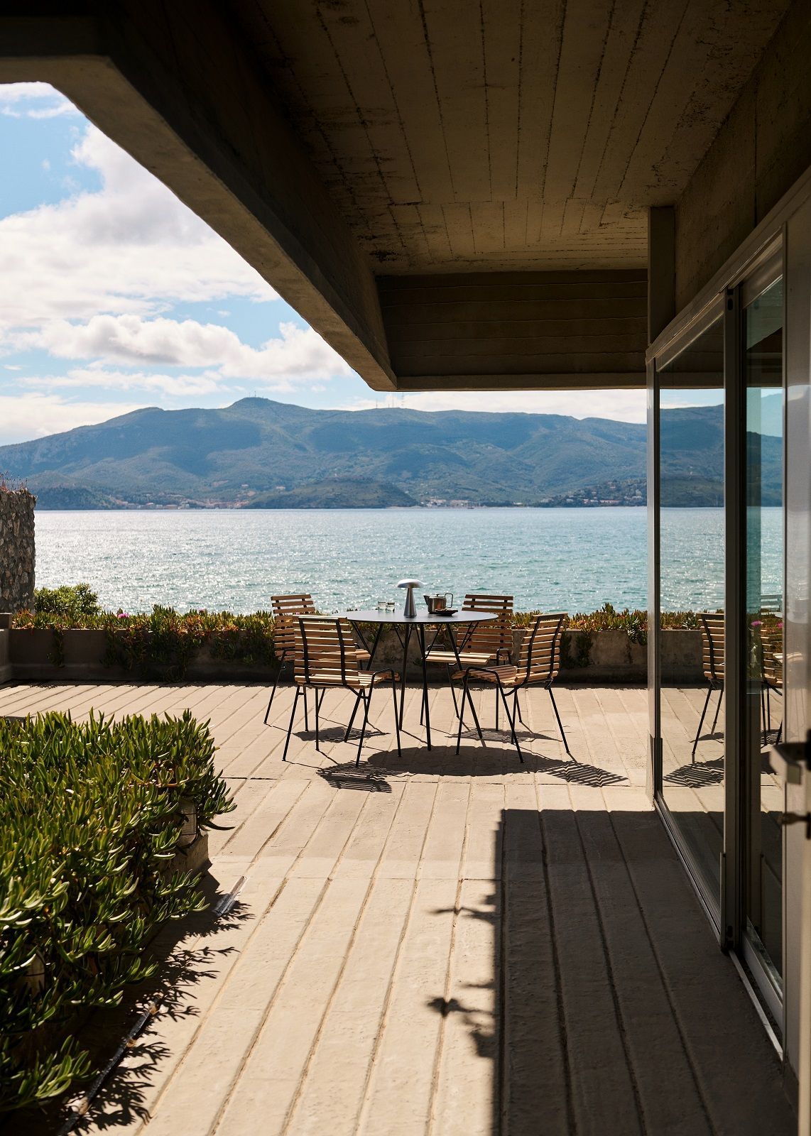 AndTradition Robin Day RD4 Outdoor Dining Chair Esszimmerstuhl auf Terrasse mit Meerblick und Bergpanorama.