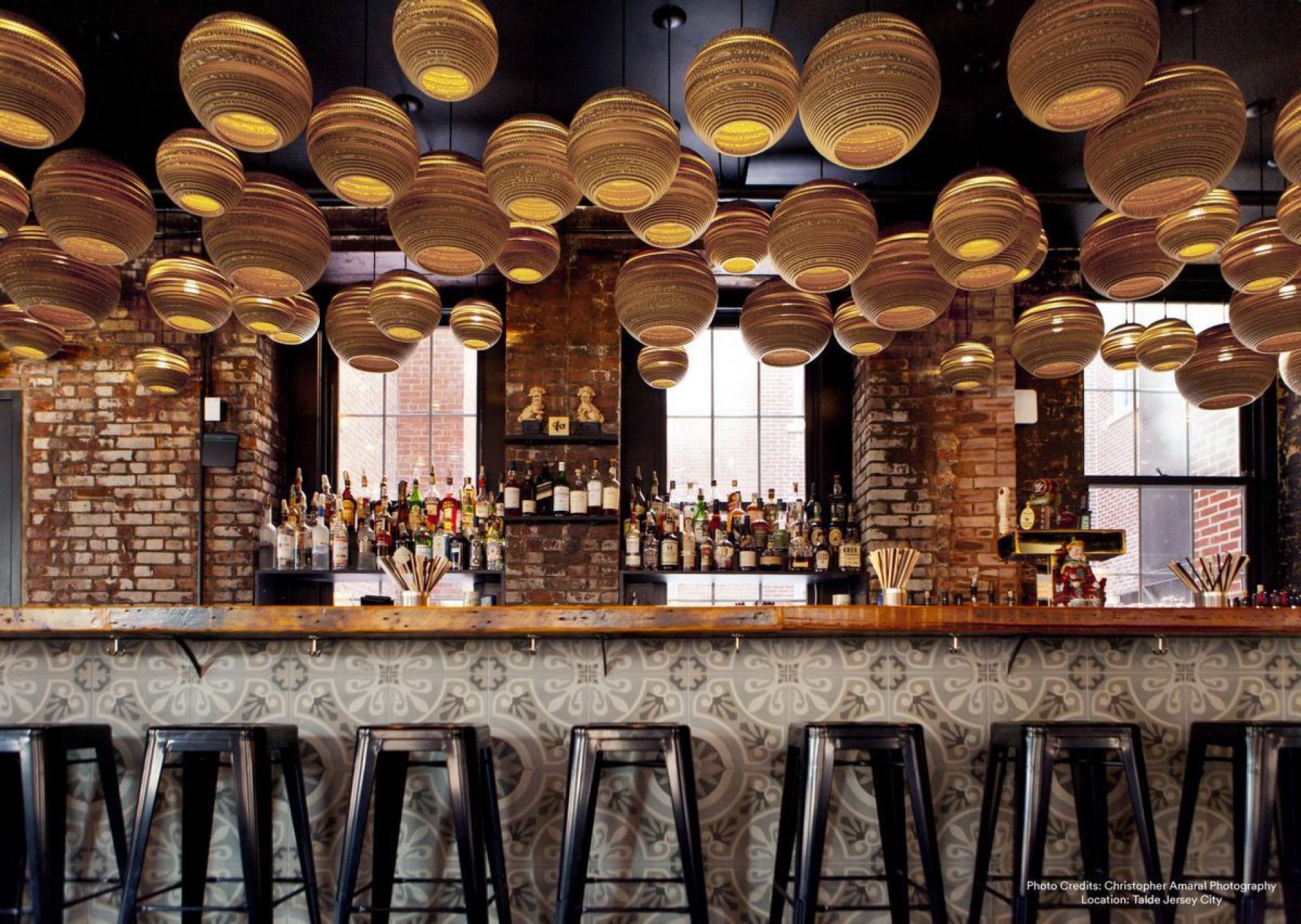 Viele Moon18 Scraplights Hängeleuchten von Graypants in einem Bar-Setting mit Backsteinwänden und Spirituosenregalen.