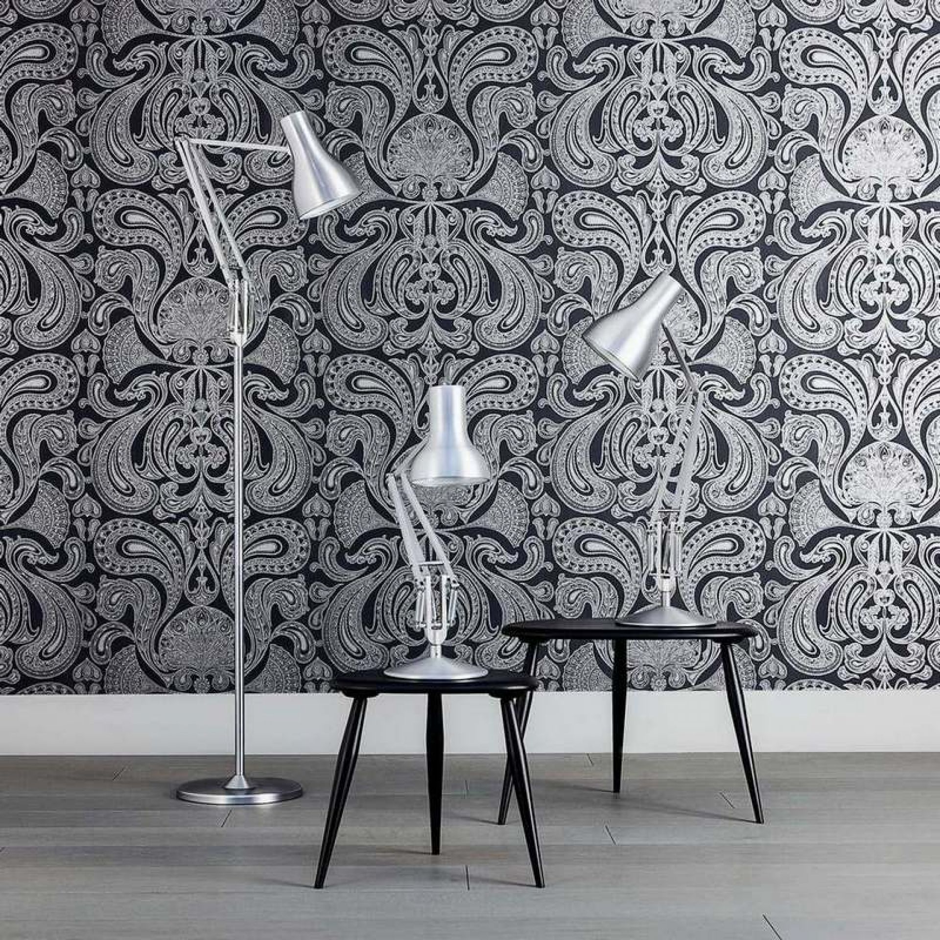 Anglepoise Type 75 Schreibtischleuchten: Stehleuchte und Tischleuchte in Silber auf schwarzen Tischen vor gemusterter Tapete.