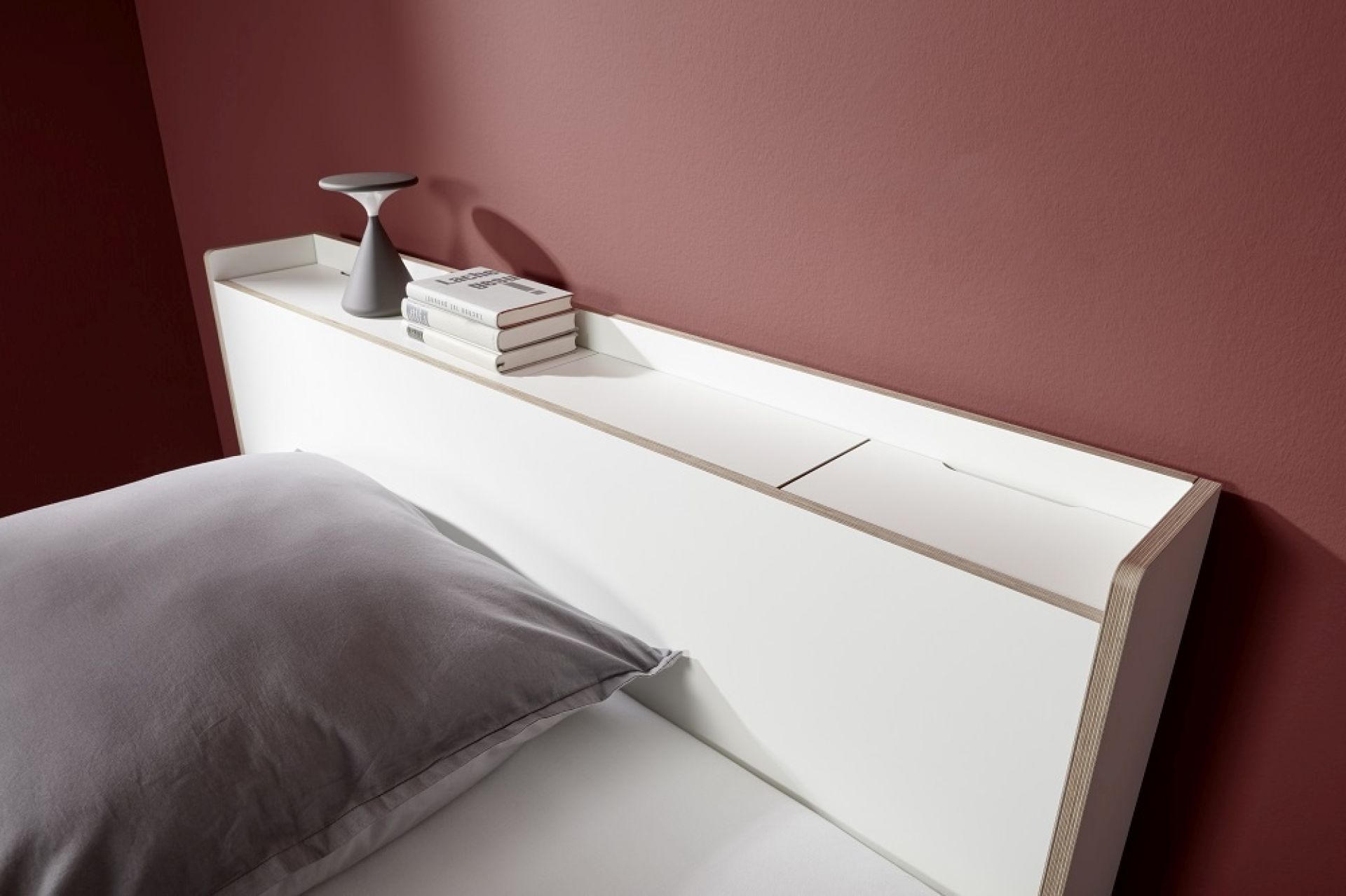 Nook Einzelbett von Müller Möbelwerkstätten mit Stauraum im weißen Kopfteil und grauem Kissen.