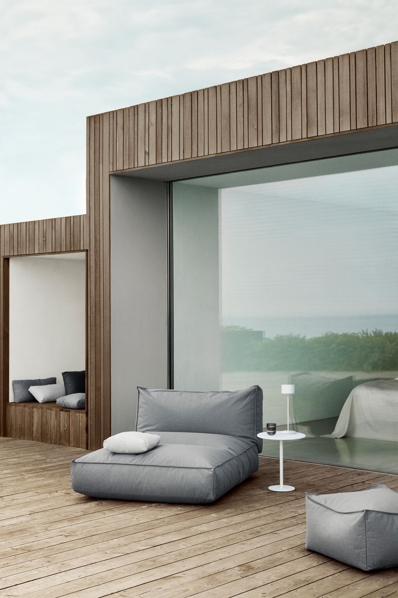 Graues STAY Kissen Outdoor von Blomus auf einer Holzterrasse mit Meerblick, minimalistisches Design.
