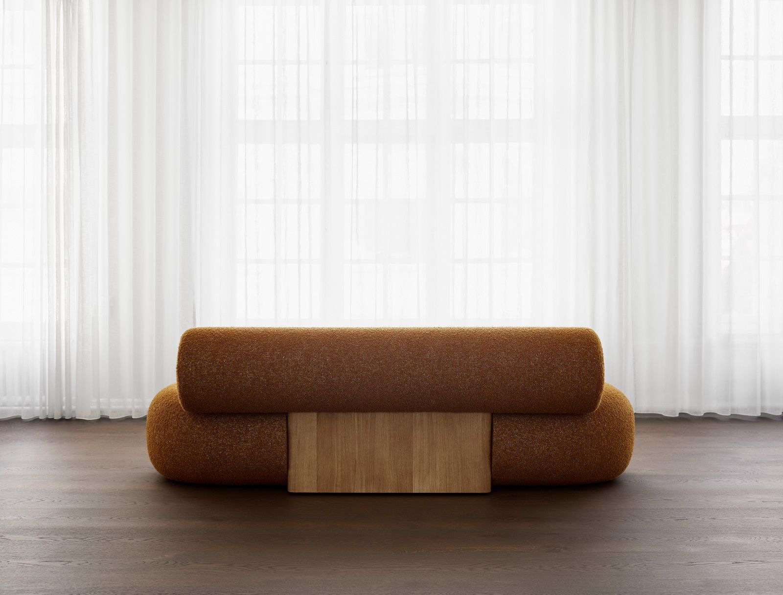 Hippo Sofa von Norr11 aus Holz mit braunem Bouclé-Stoff und hellem Holzsockel vor Fenster.