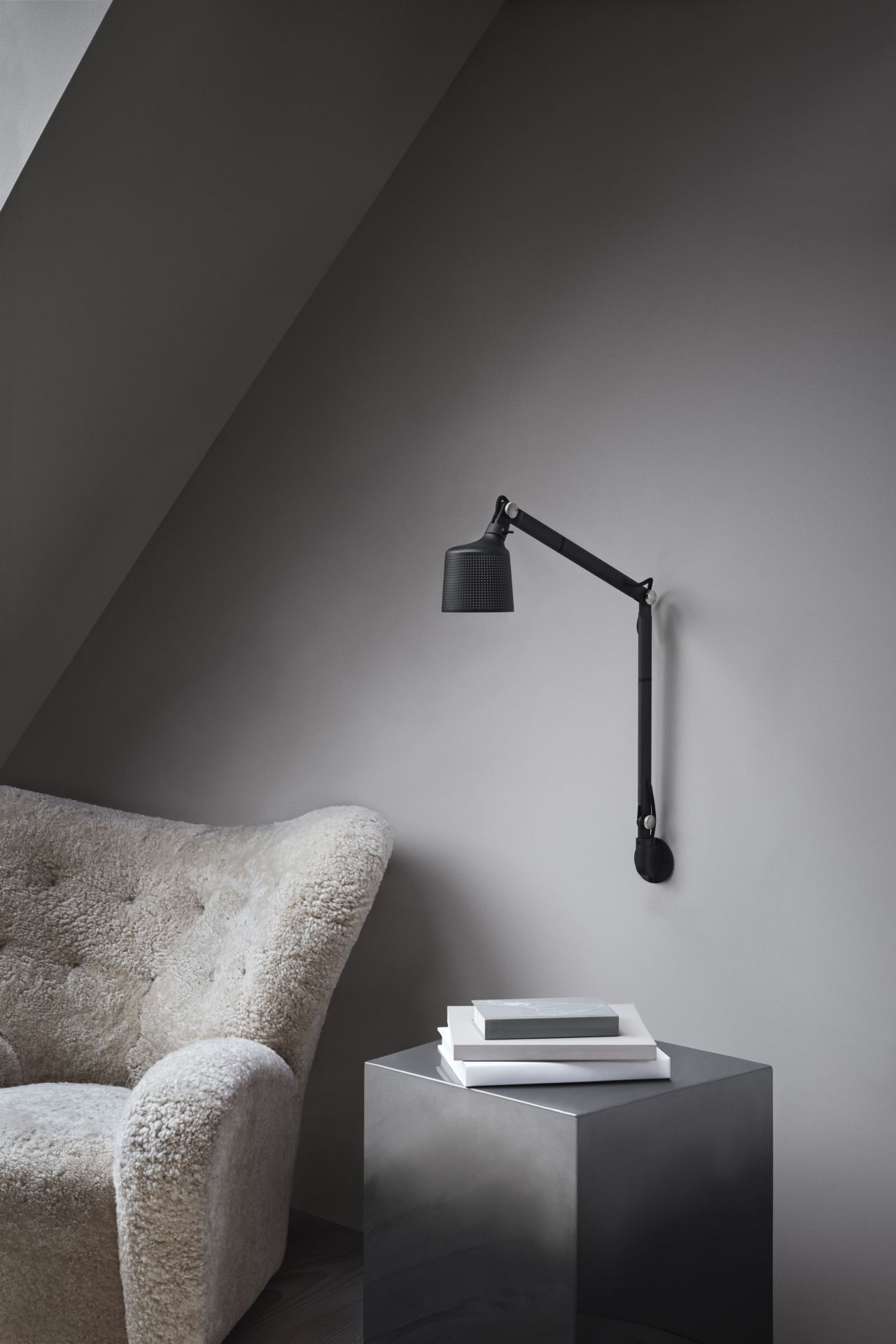 Nahaufnahme einer schwarzen Vipp Wandlampe über einem Nachttisch mit Büchern neben einem Sessel.