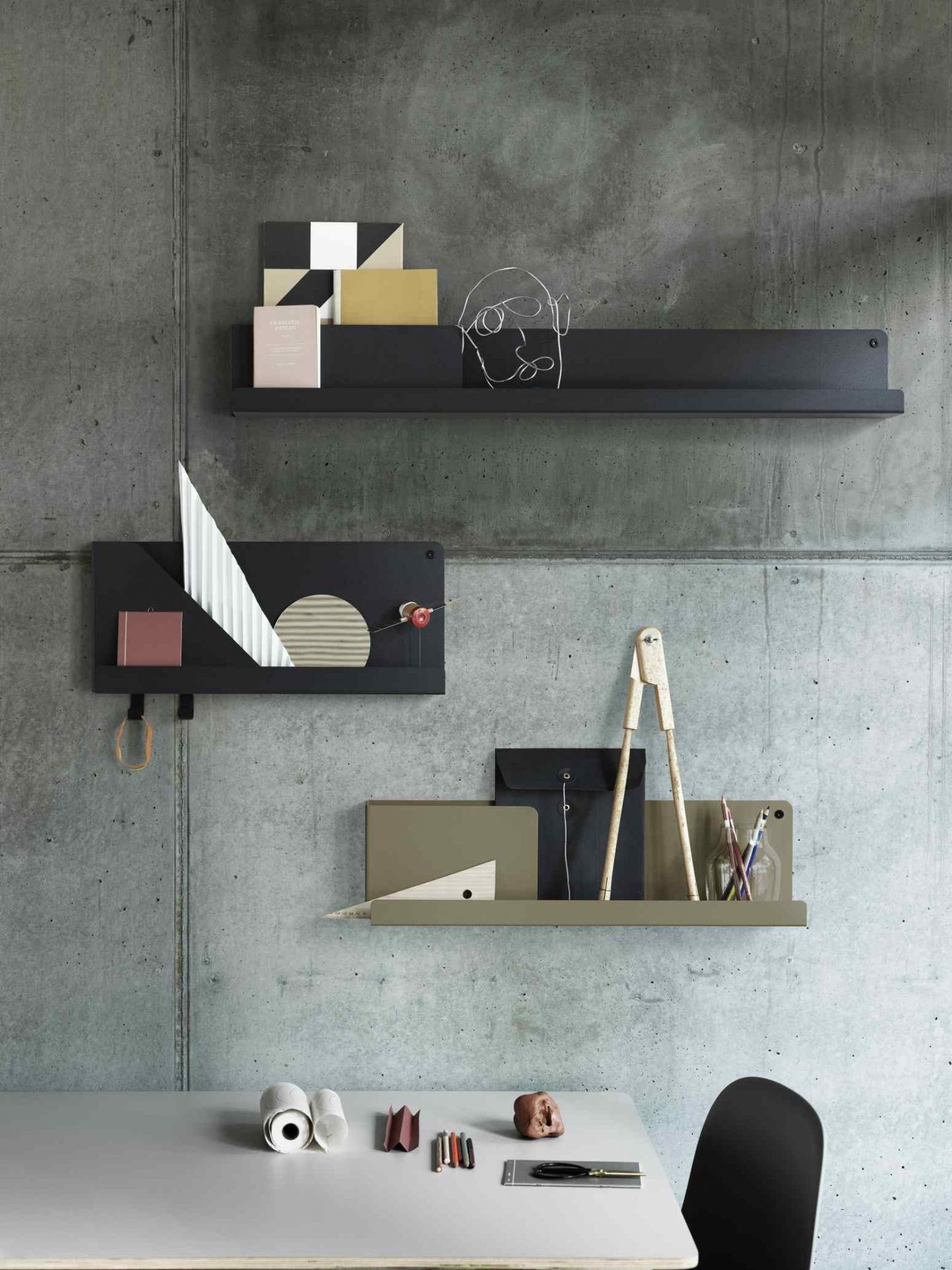 Muuto Folded Shelves Wandregal in Schwarz und Olivgrün an einer Betonwand mit Dekoration.