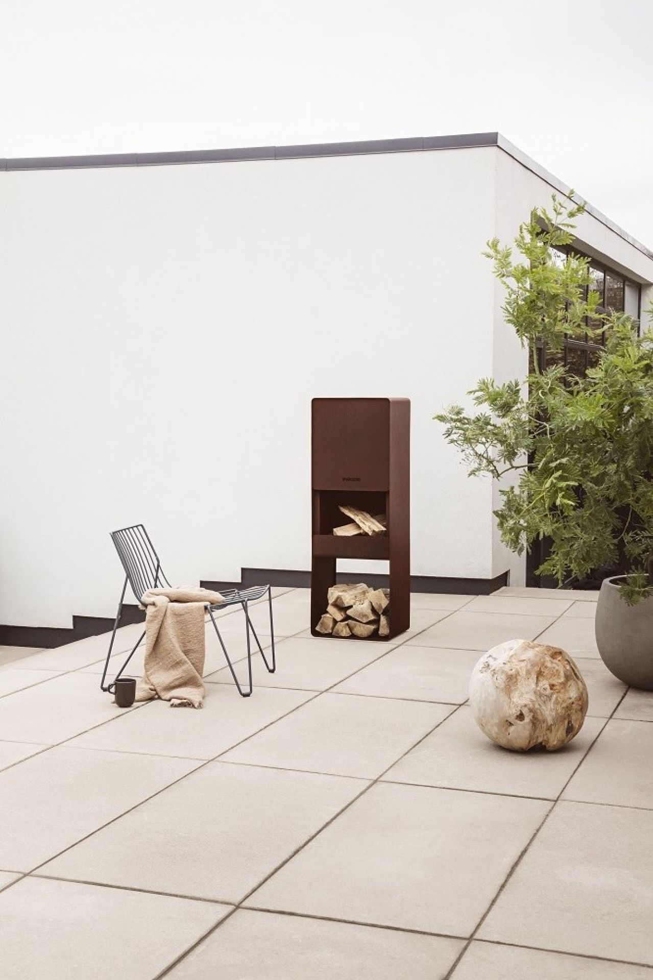 Eva Solo FireBox Gartenkamin aus Stahl mit Holzscheiten auf einer Terrasse.